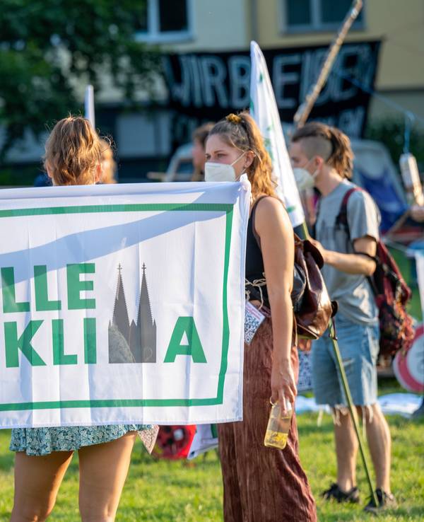 Eine Aktivistin hält bei einer Demonstration die „Kölle fürs Klima“-Flagge nach oben.