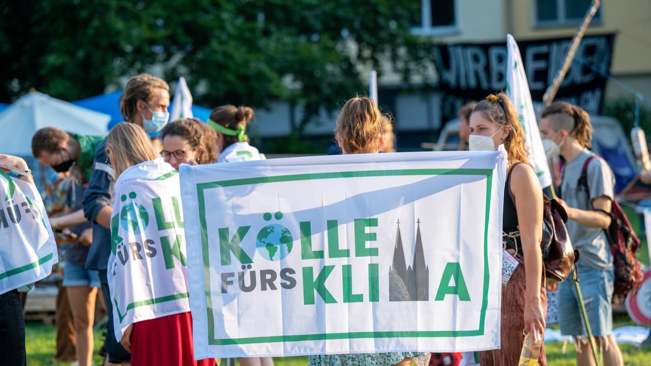 Eine Aktivistin hält bei einer Demonstration die „Kölle fürs Klima“-Flagge nach oben.