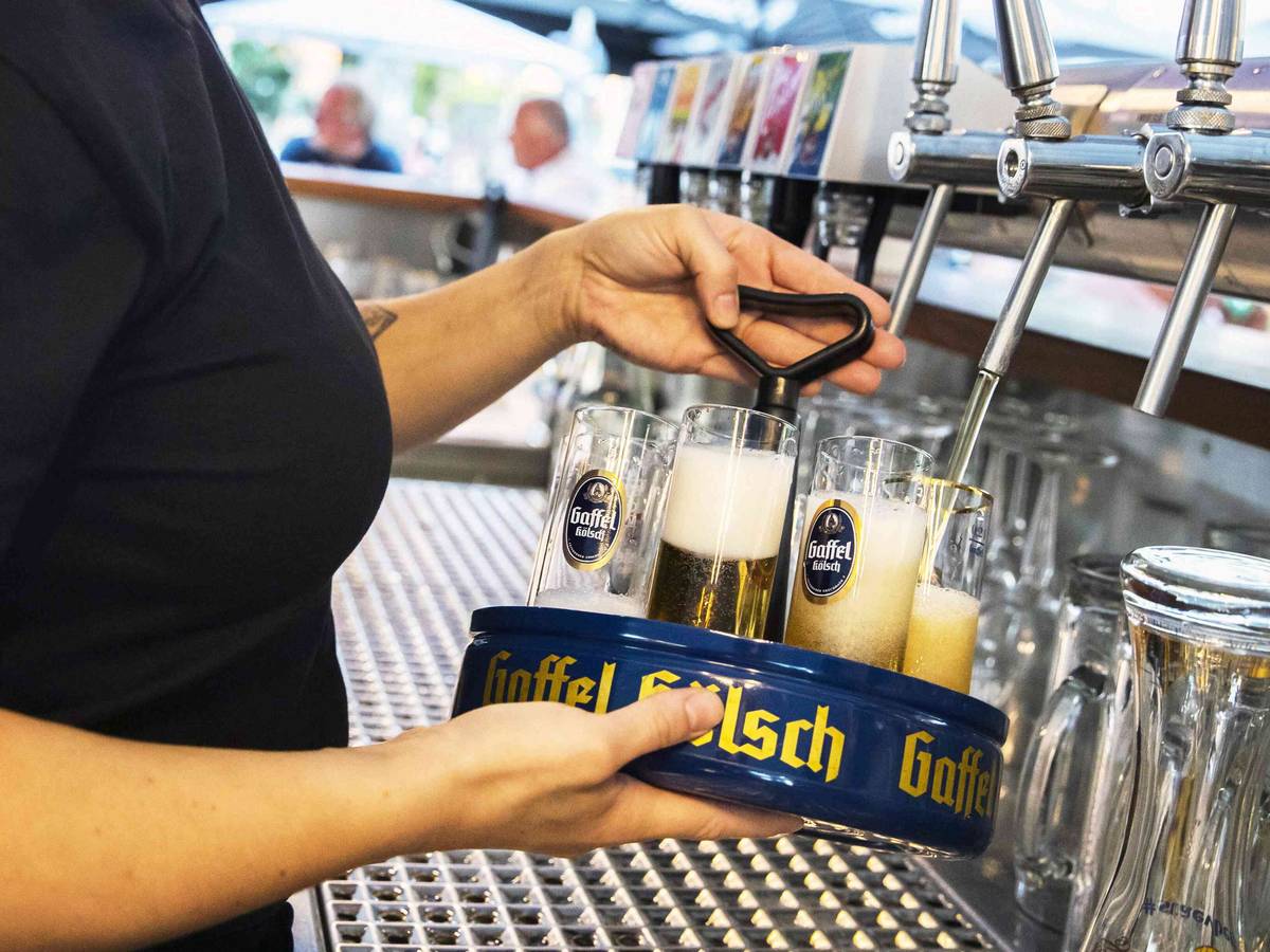 Eine Köbine zapft Gaffel-Kölsch in einem Biergarten.