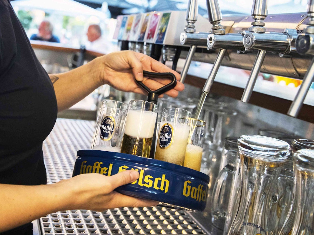 Eine Köbine zapft Gaffel-Kölsch in einem Biergarten.