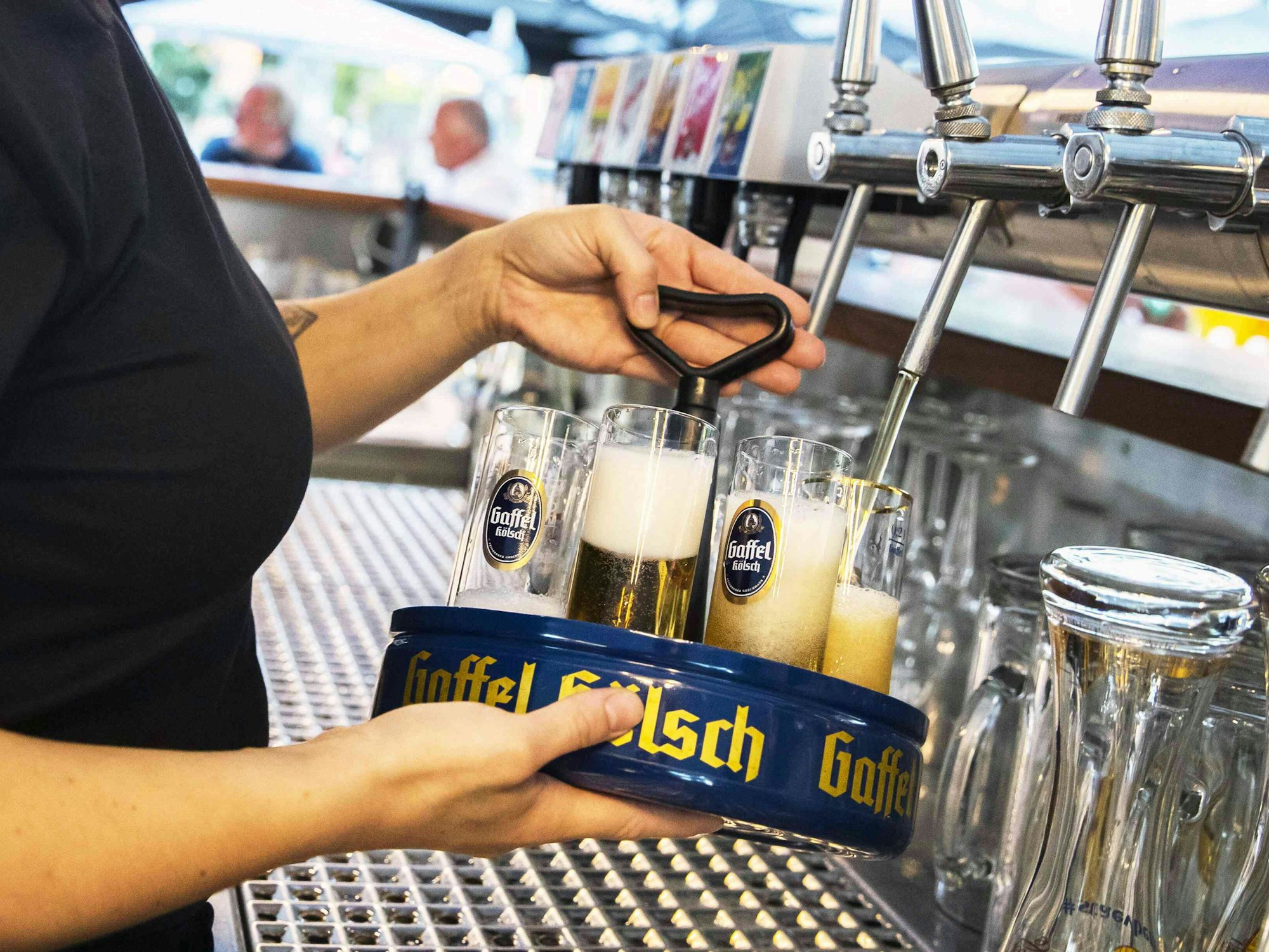In einem Biergarten wird von einer Kellnerin ein Kranz Kölsch gezapft.