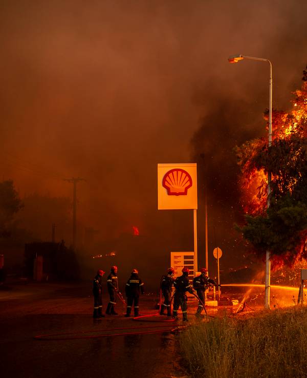 Feuerwehrleute bekämpfen einen Waldbrand in einem Waldgebiet nördlich von Athen, welches sich einer Tankstelle nähert.