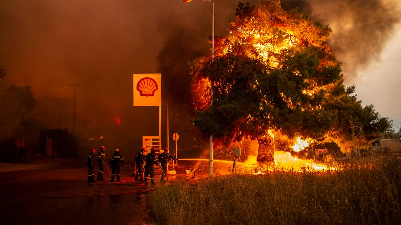 Feuerwehrleute bekämpfen einen Waldbrand in einem Waldgebiet nördlich von Athen, welches sich einer Tankstelle nähert.