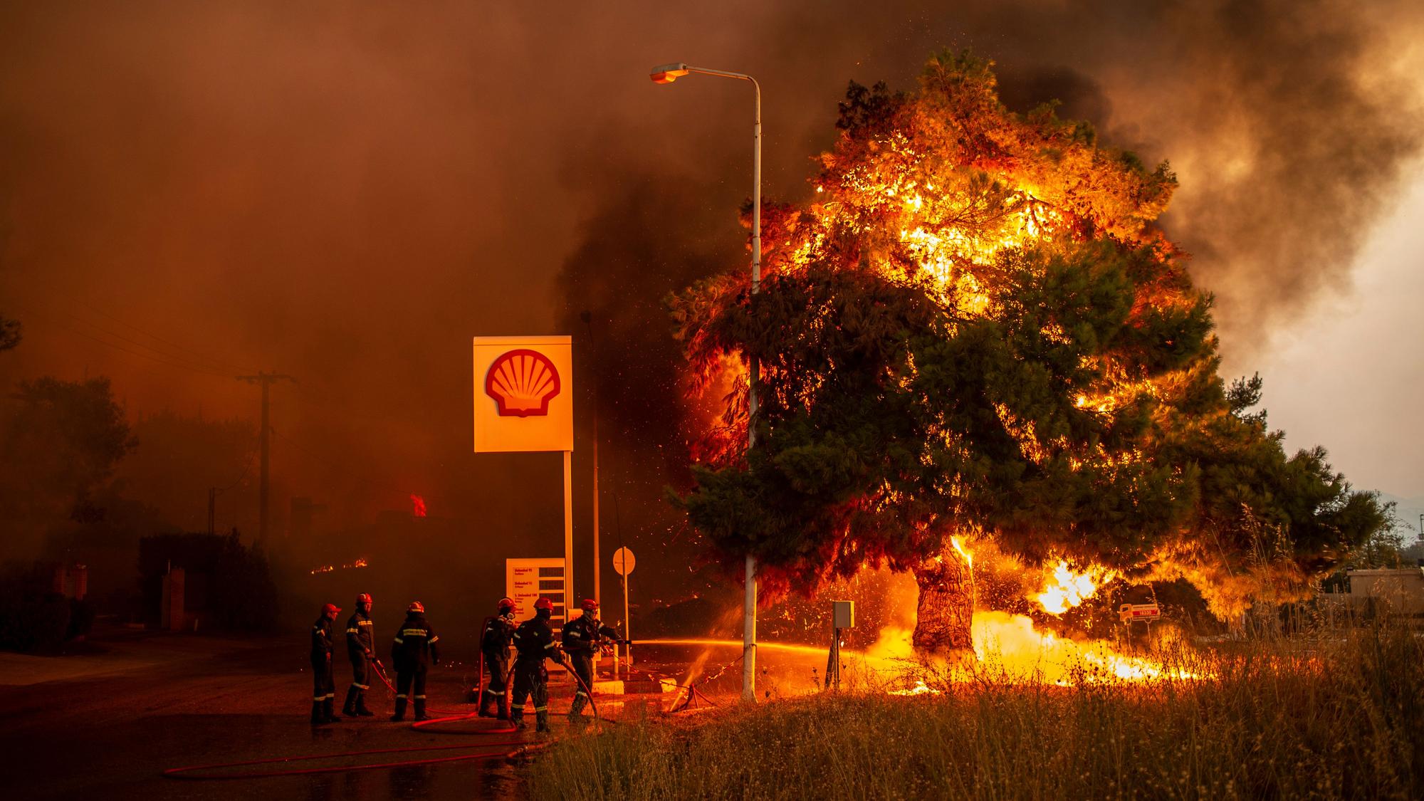 Feuerwehrleute bekämpfen einen Waldbrand in einem Waldgebiet nördlich von Athen, welches sich einer Tankstelle nähert.