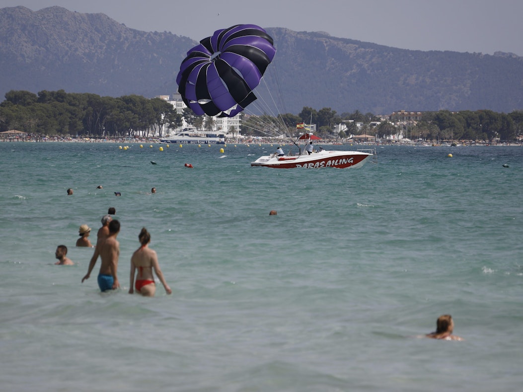 Menschen baden im Meer am Playa de Muro, im Hintergrund Berge und Felsen.
