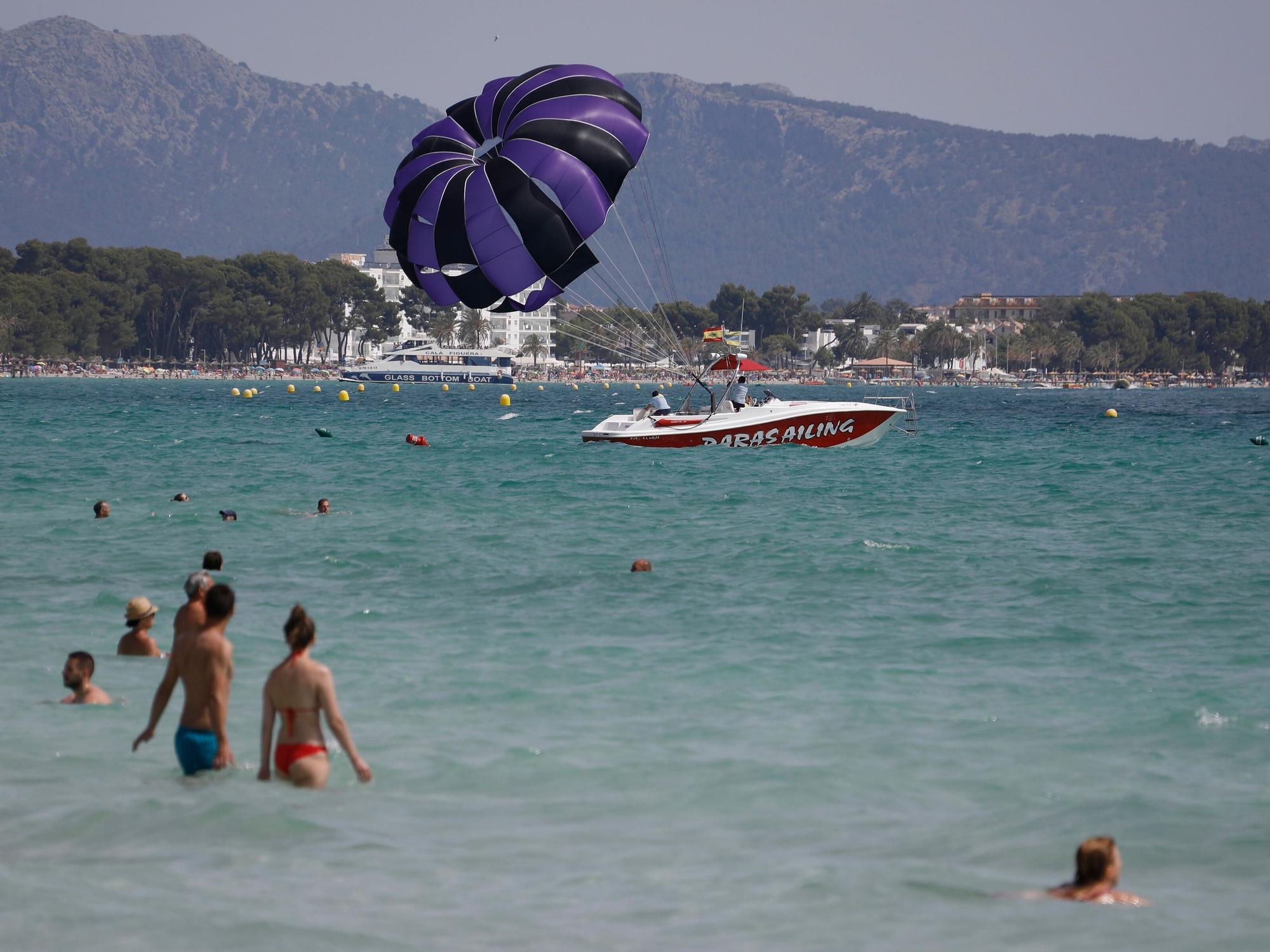 Menschen baden im Meer am Playa de Muro, im Hintergrund Berge und Felsen.