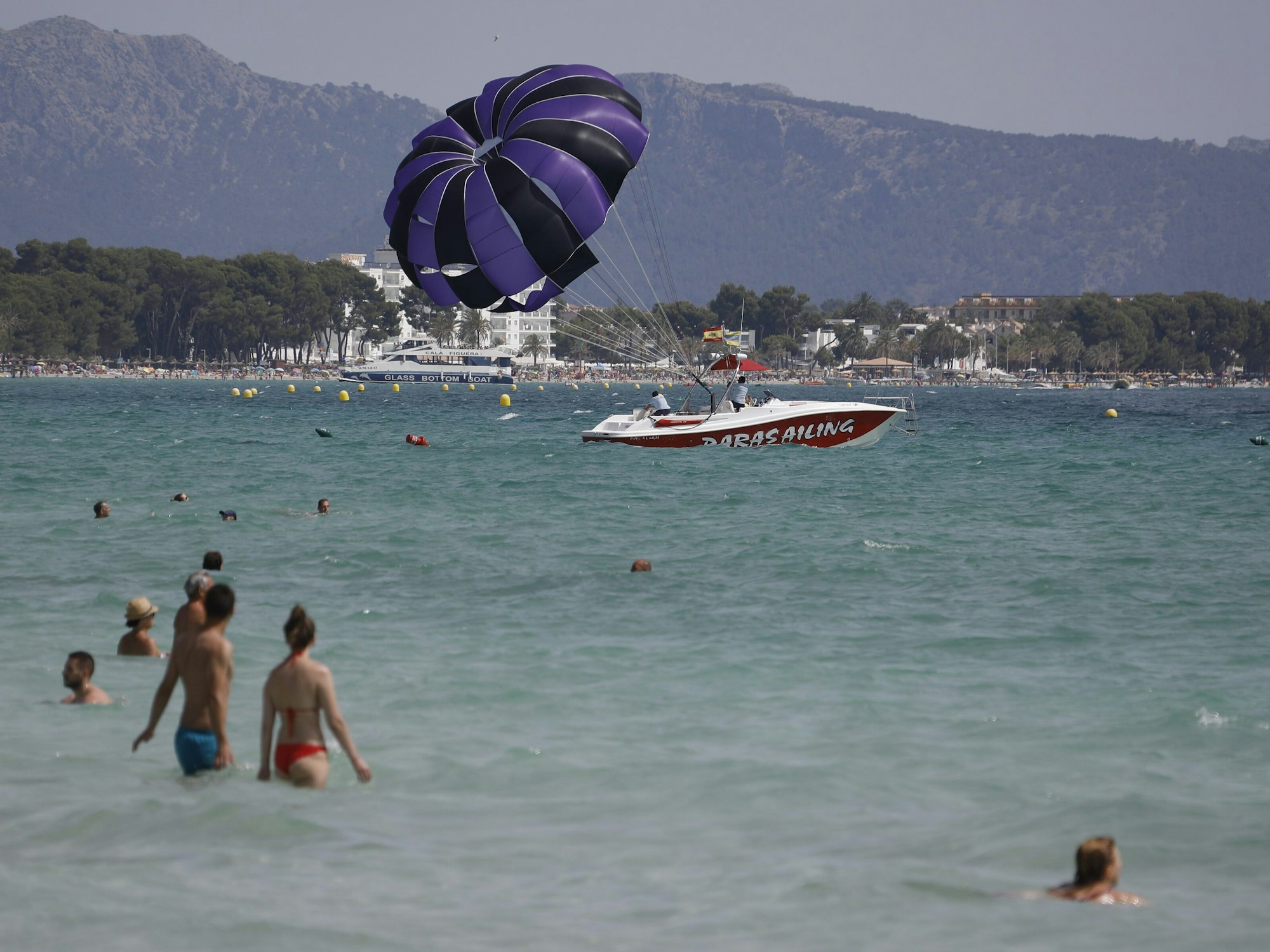 Menschen baden im Meer am Playa de Muro, im Hintergrund Berge und Felsen.