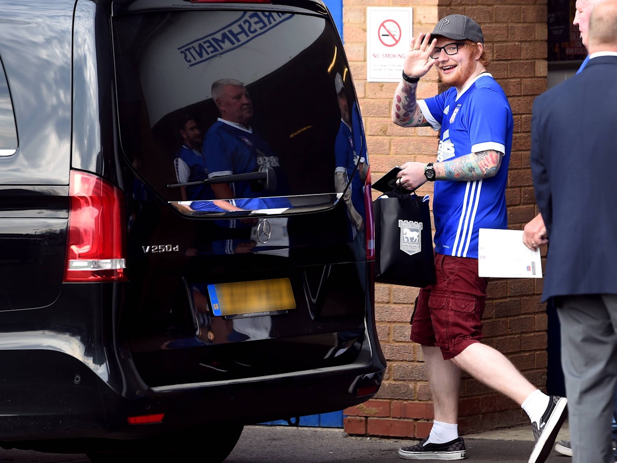 Ed Sheeran winkt mit einem Trikot des englischen Drittligisten Ipswich Town in die Kamera.
