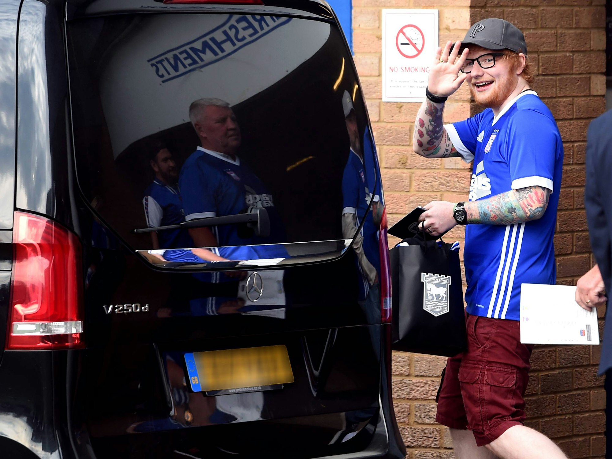 Ed Sheeran winkt mit einem Trikot des englischen Drittligisten Ipswich Town in die Kamera.