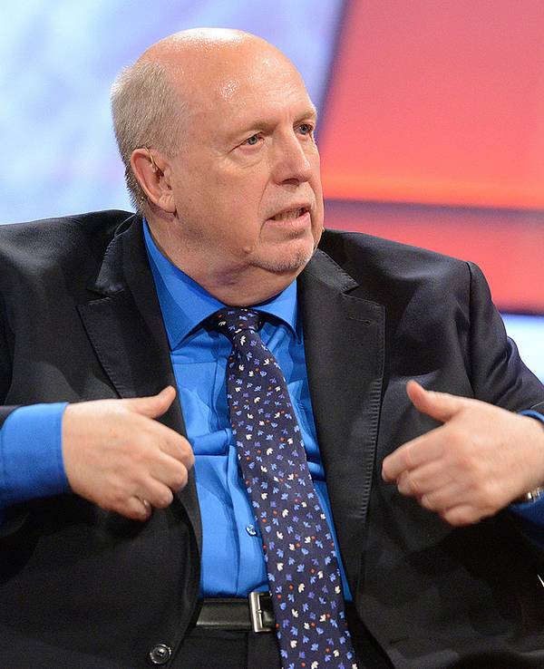 Reiner Calmund gestikuliert mit den Händen, während er in einer TV-Show auf einer Couch sitzt.