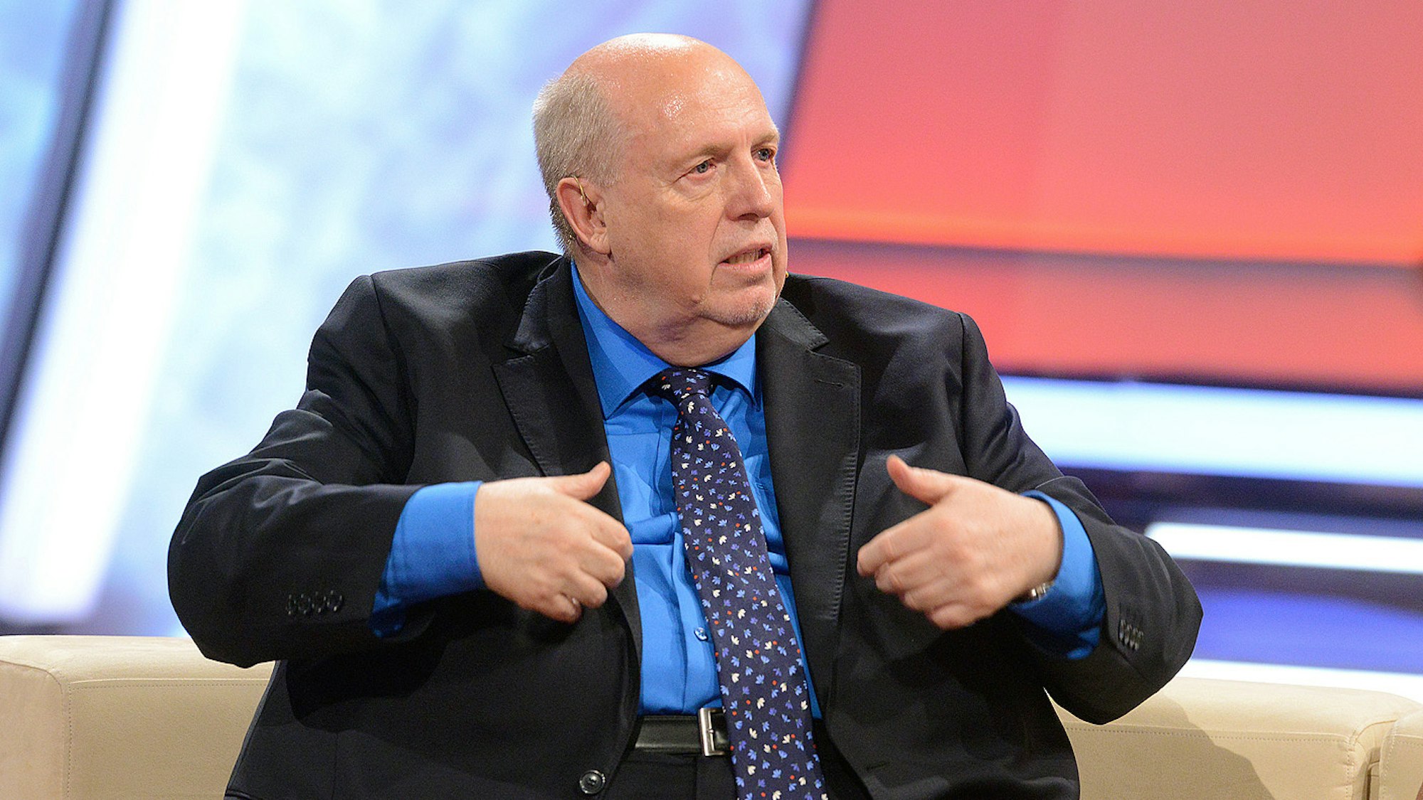 Reiner Calmund gestikuliert mit den Händen, während er in einer TV-Show auf einer Couch sitzt.
