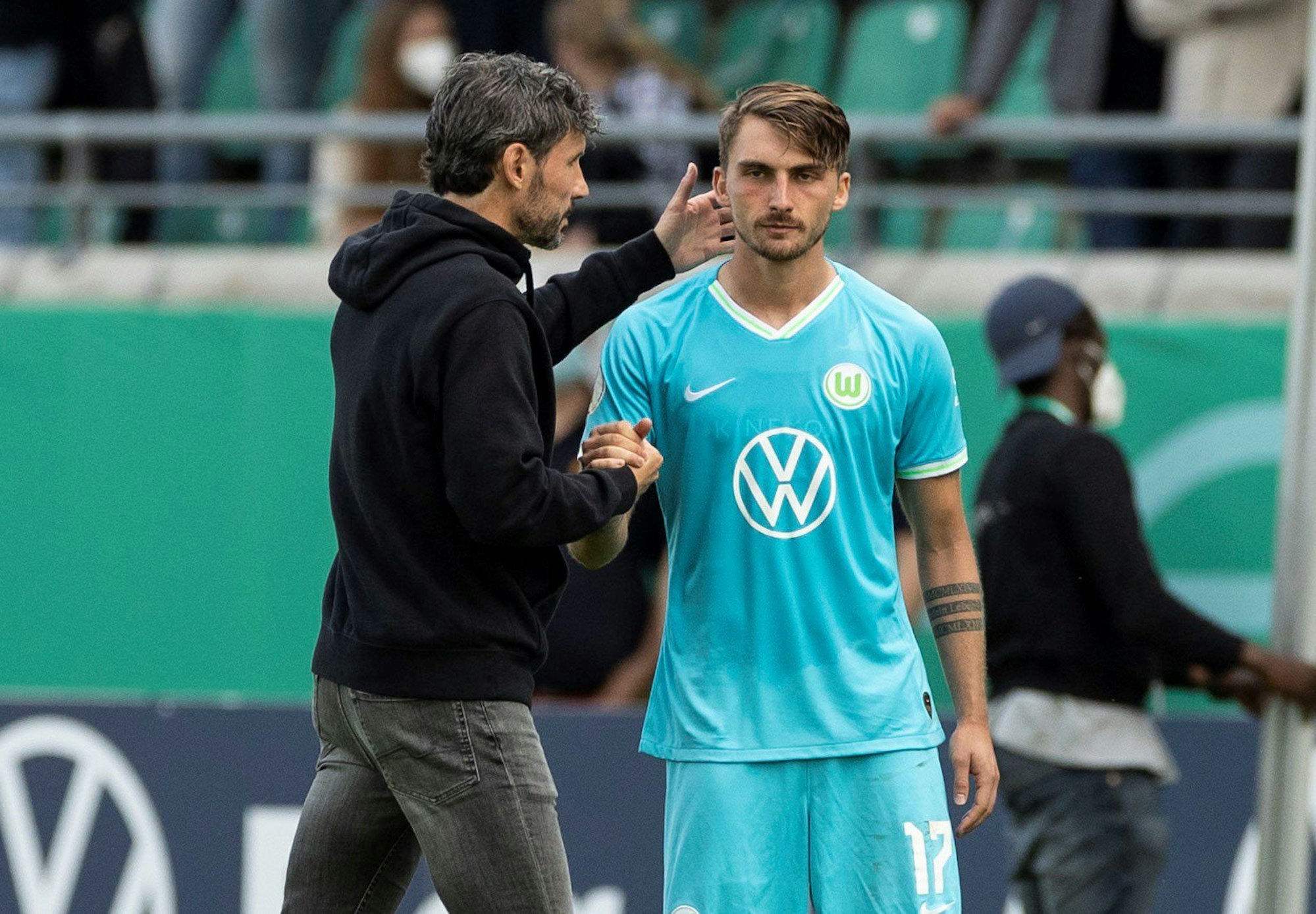 Wolfsburgs Trainer Mark van Bommel (l) steht vor der Einwechslung mit Maximilian Philipp zusammen.