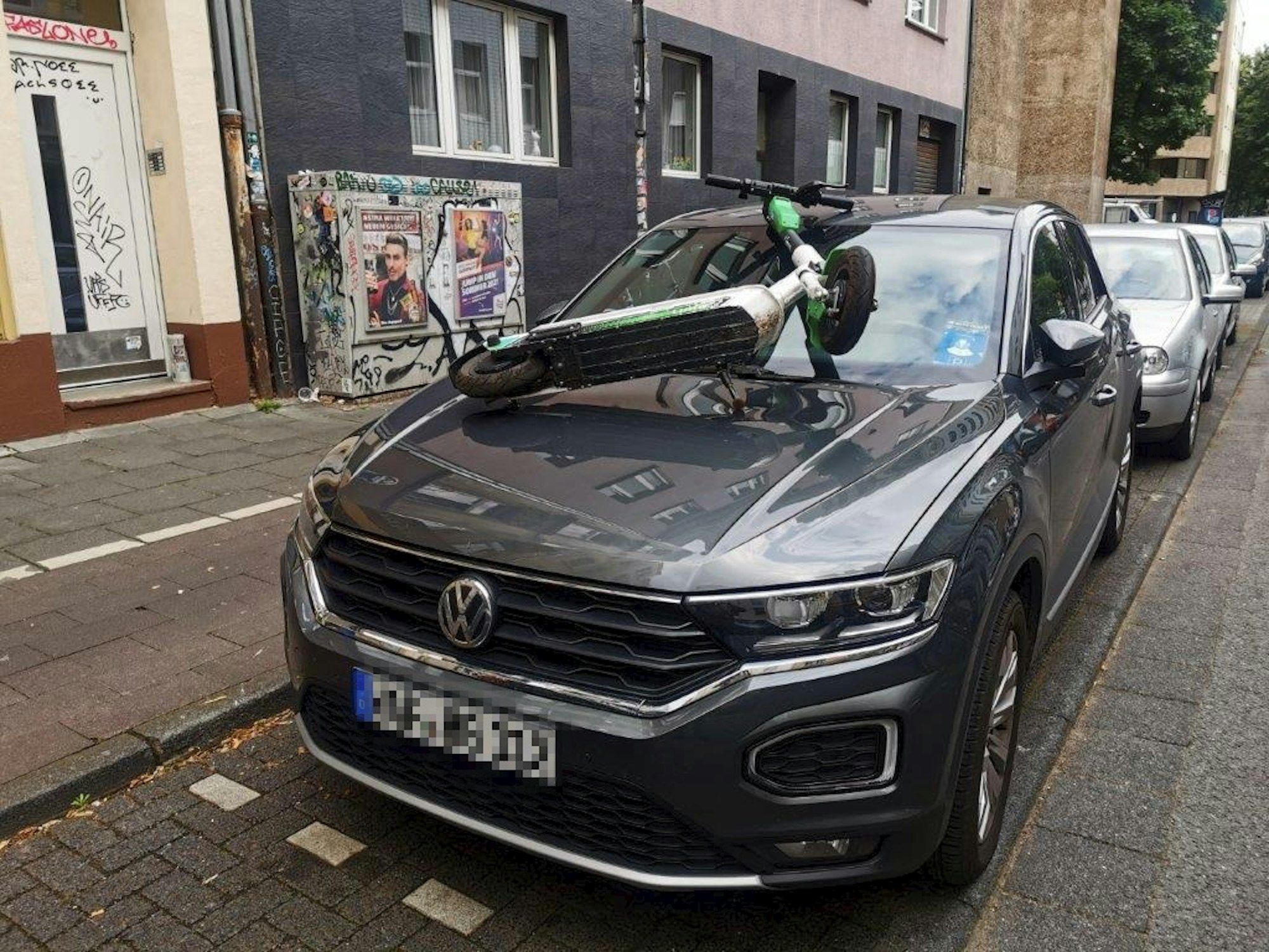 Ein E-Scooter liegt auf der Windschutzscheibe eines Autos.