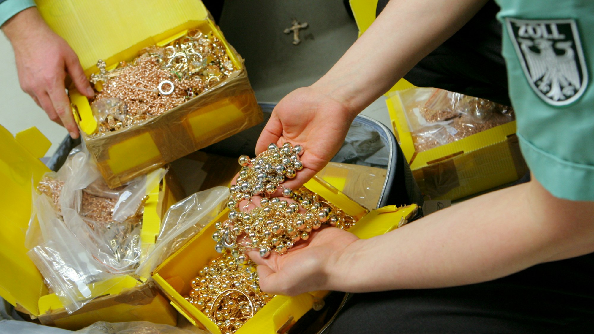 Zwei Zollbeamte zeigen geschmuggelten Goldschmuck aus einem Koffer.