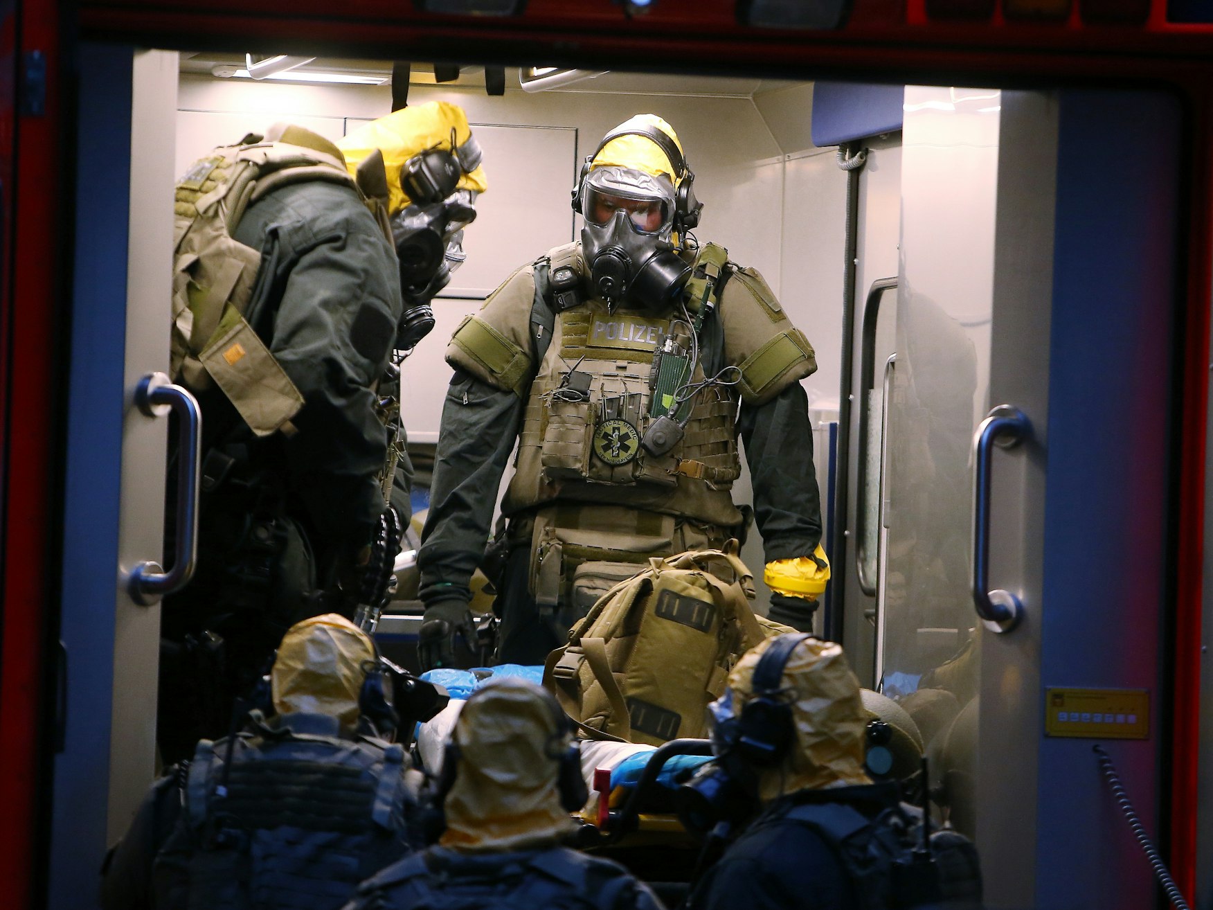 SEK Beamten mit Atemschutzmasken und Schutzanzügen stehen in einem Fahrzeug vor einem Kölner Wohnkomplex.