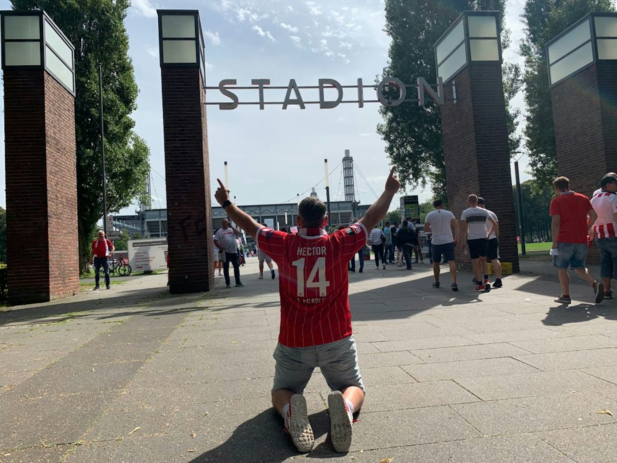 Express-Redakteur Bastian Ebel kniet mit beiden Fingern in Richtung Himmel vor dem Rhein-Energie-Stadion.