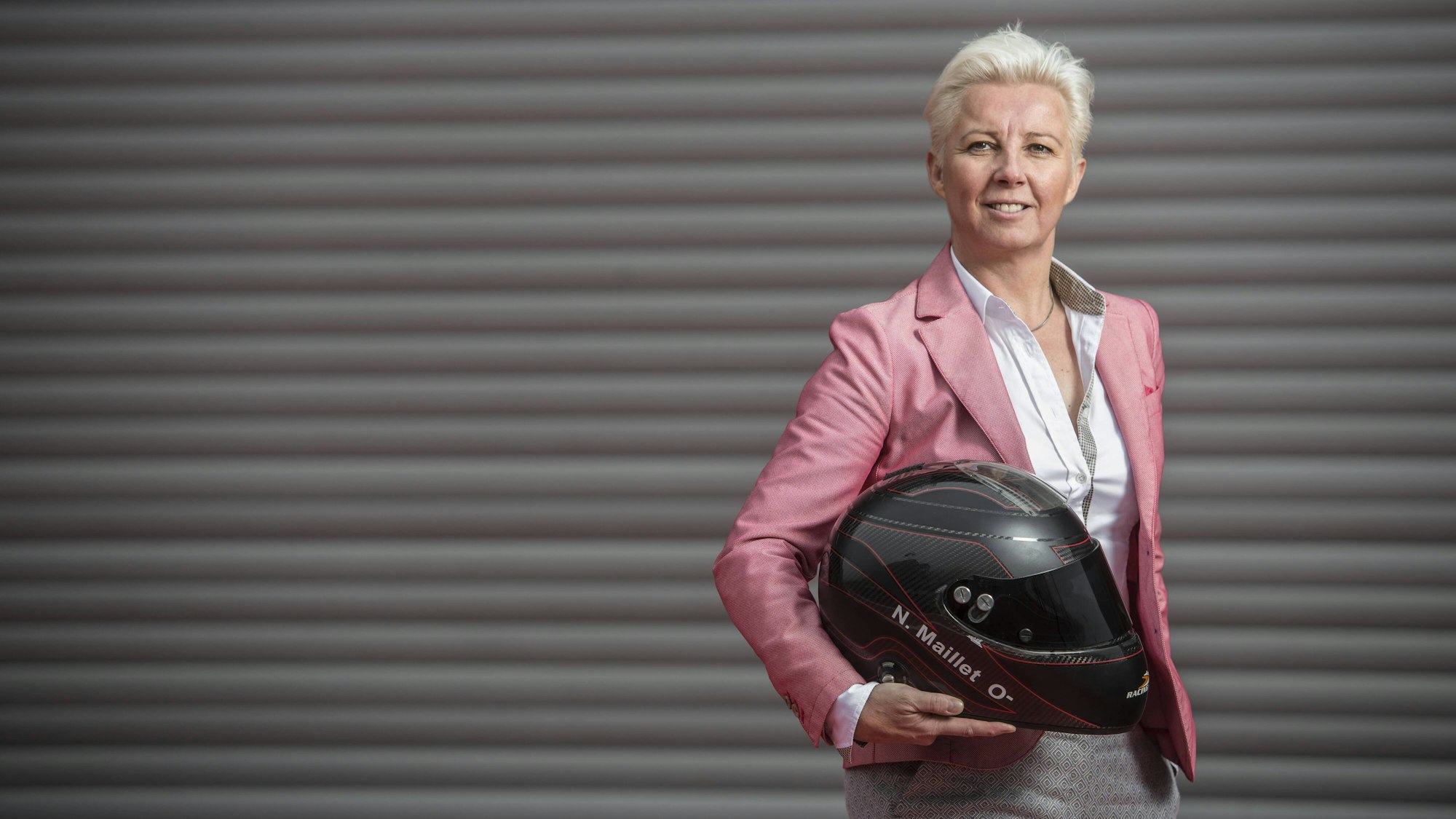 Nathalie Maillet hält einen Motorsport-Helm in der Hand und lächelt in die Kamera.