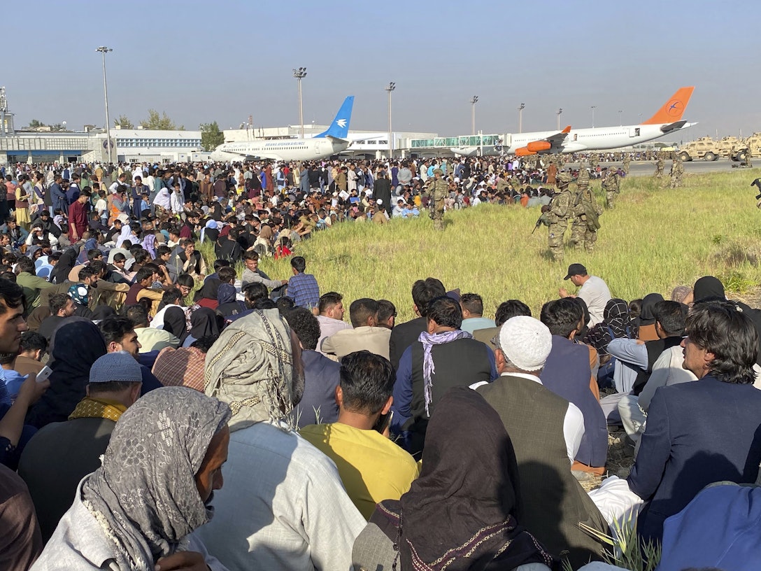 US-Soldaten bewachen eine Absperrung am Flughafen, davor drängeln sich Tausende Menschen.