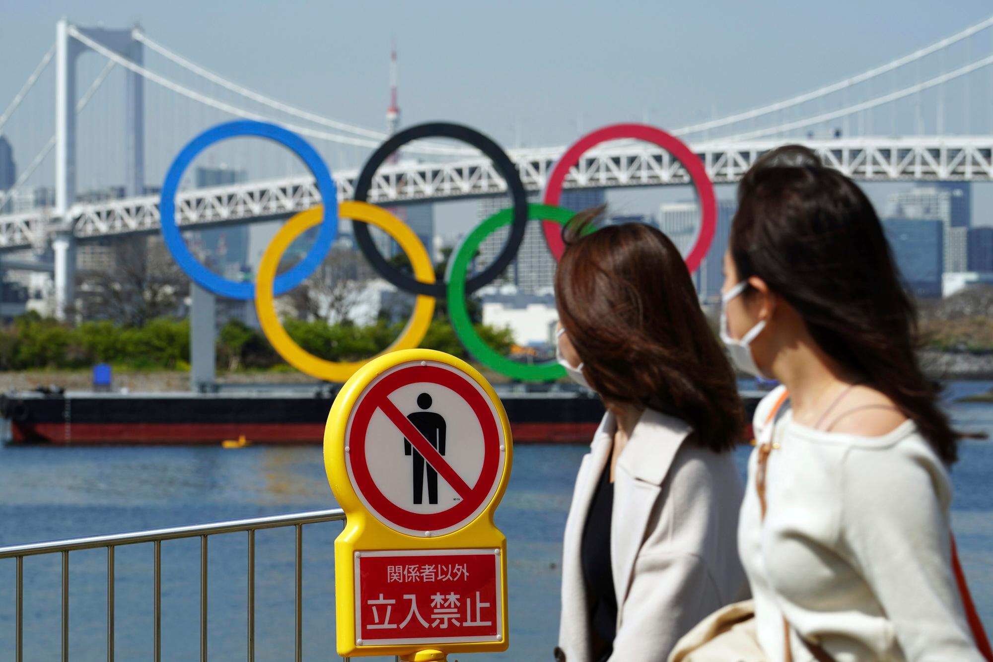 Zwei Frauen gehen an einem „Betreten verboten“-Schild vorbei. Dahinter sind die Olympischen Ringe zu sehen.