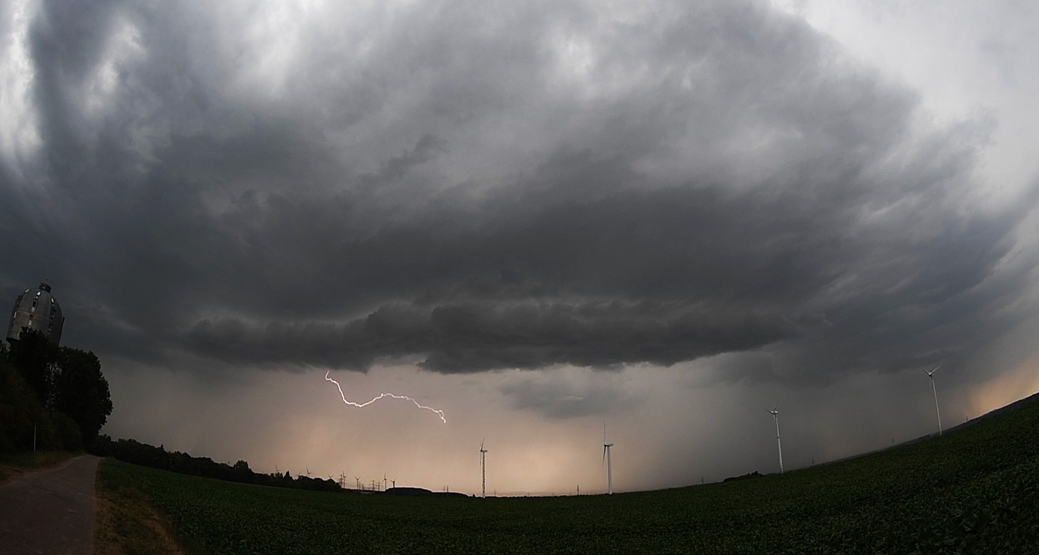 Eine Unwetterfront mit Blitzschlag zieht über ein Feld mit Windrädern hinweg.