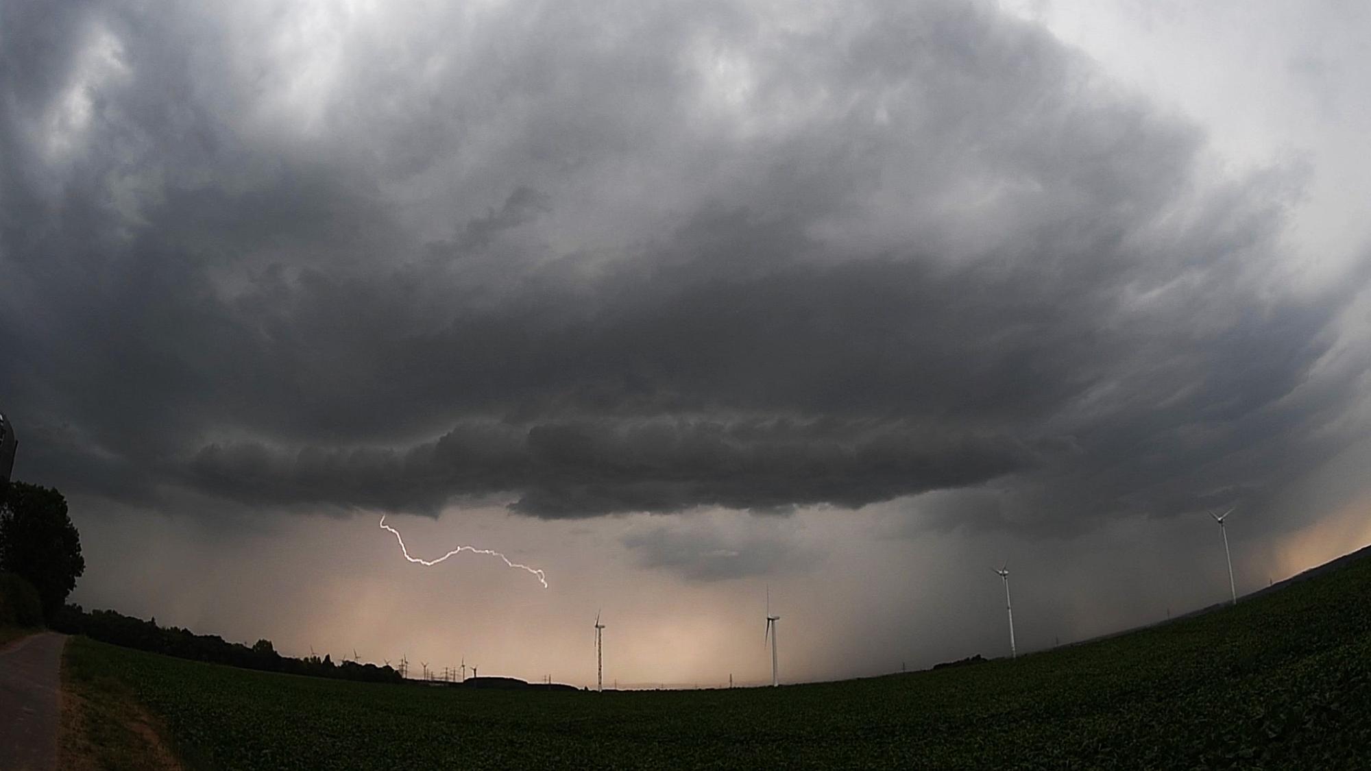 Eine Unwetterfront mit Blitzschlag zieht über ein Feld mit Windrädern hinweg.