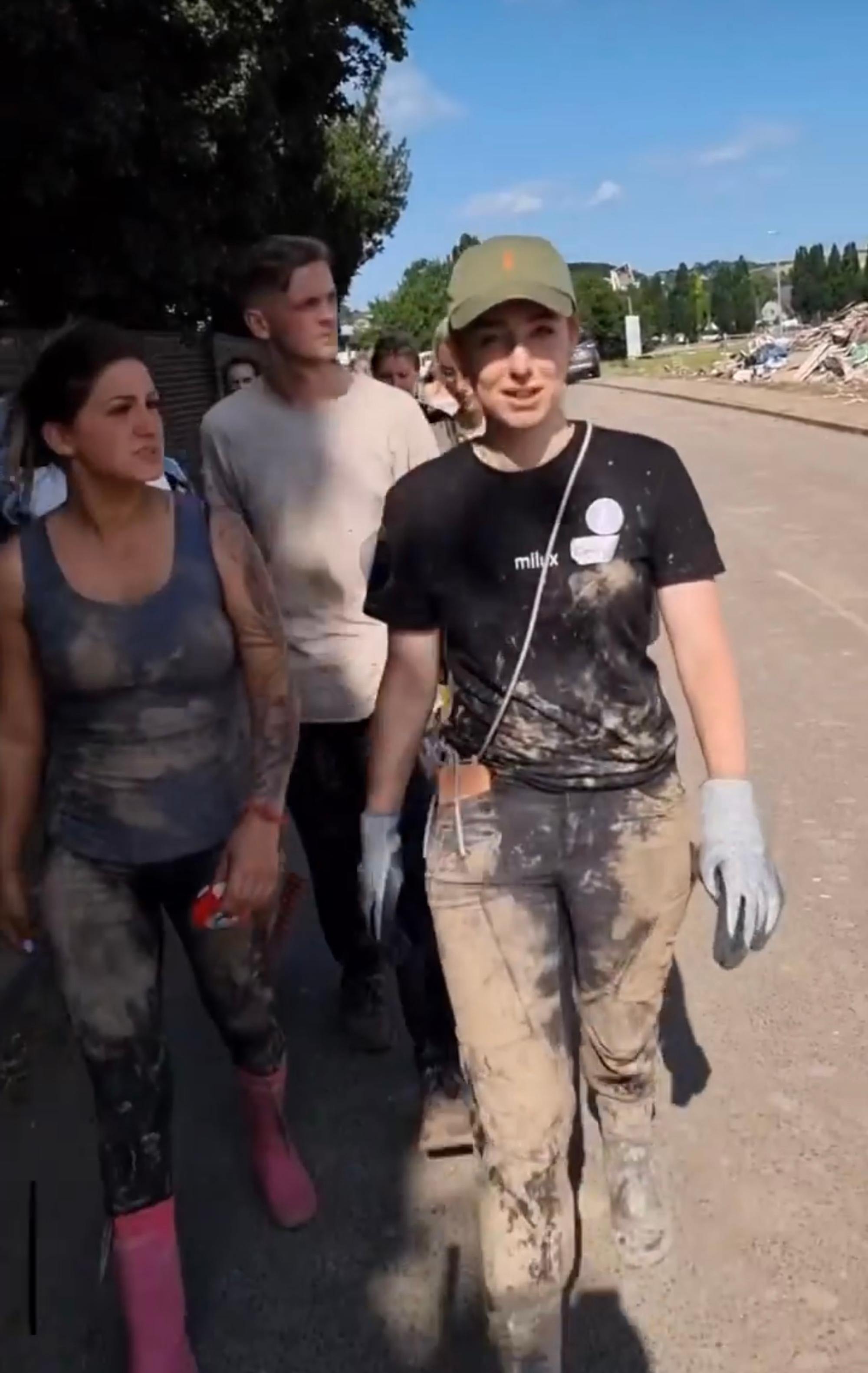 Emily mit verschlammten Klamotten und Handschuhen mit zwei weiteren Helfenden.