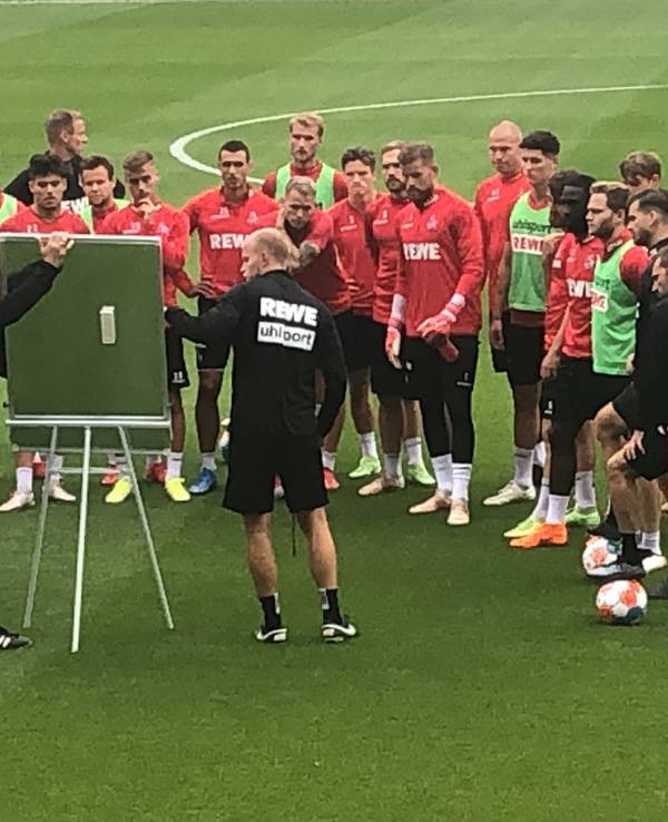 Steffen Baumgart und Assistent Kevin McKenna versammeln die Mannschaft im Training des 1. FC Köln vor der Taktiktafel.