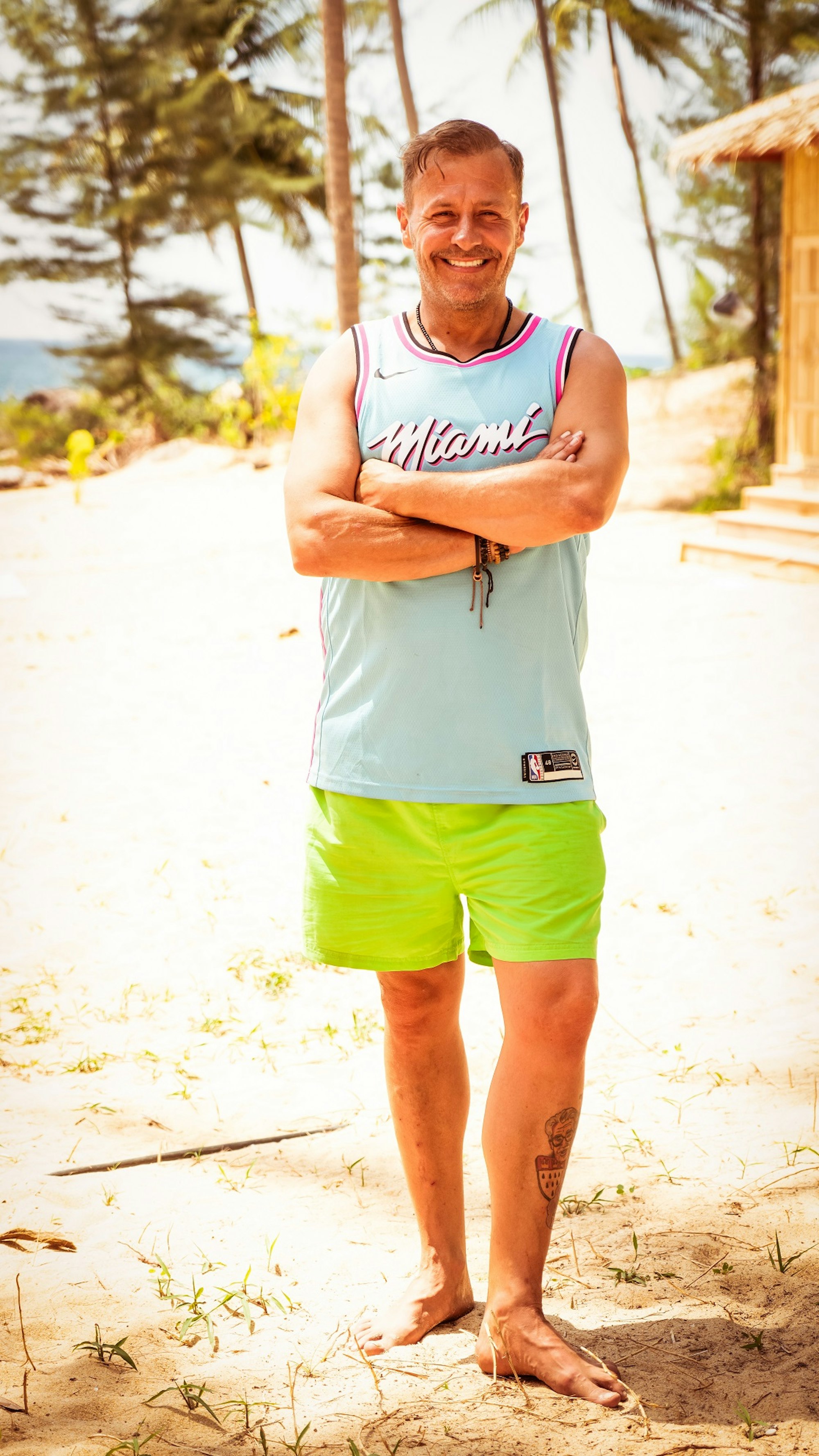 Willi Herren steht mit verschränkten Armen und breitem Lächeln am Strand von „Kampf der Realitystars“.