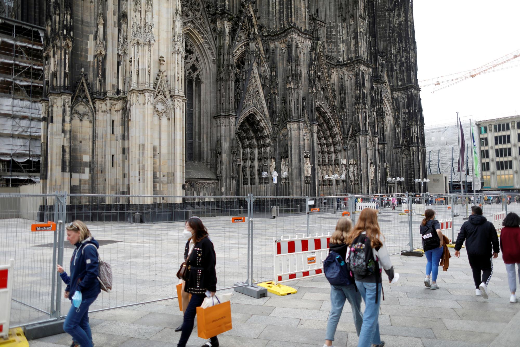 Menschen gehen auf der Domplatte an einer Absperrung vorbei.