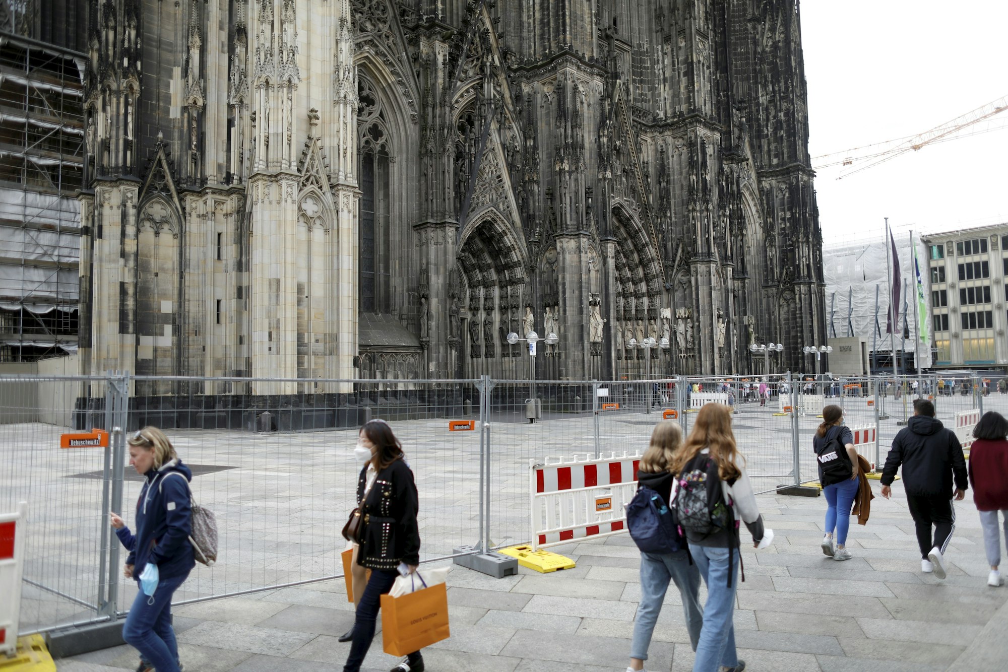 Menschen gehen auf der Domplatte an einer Absperrung vorbei.