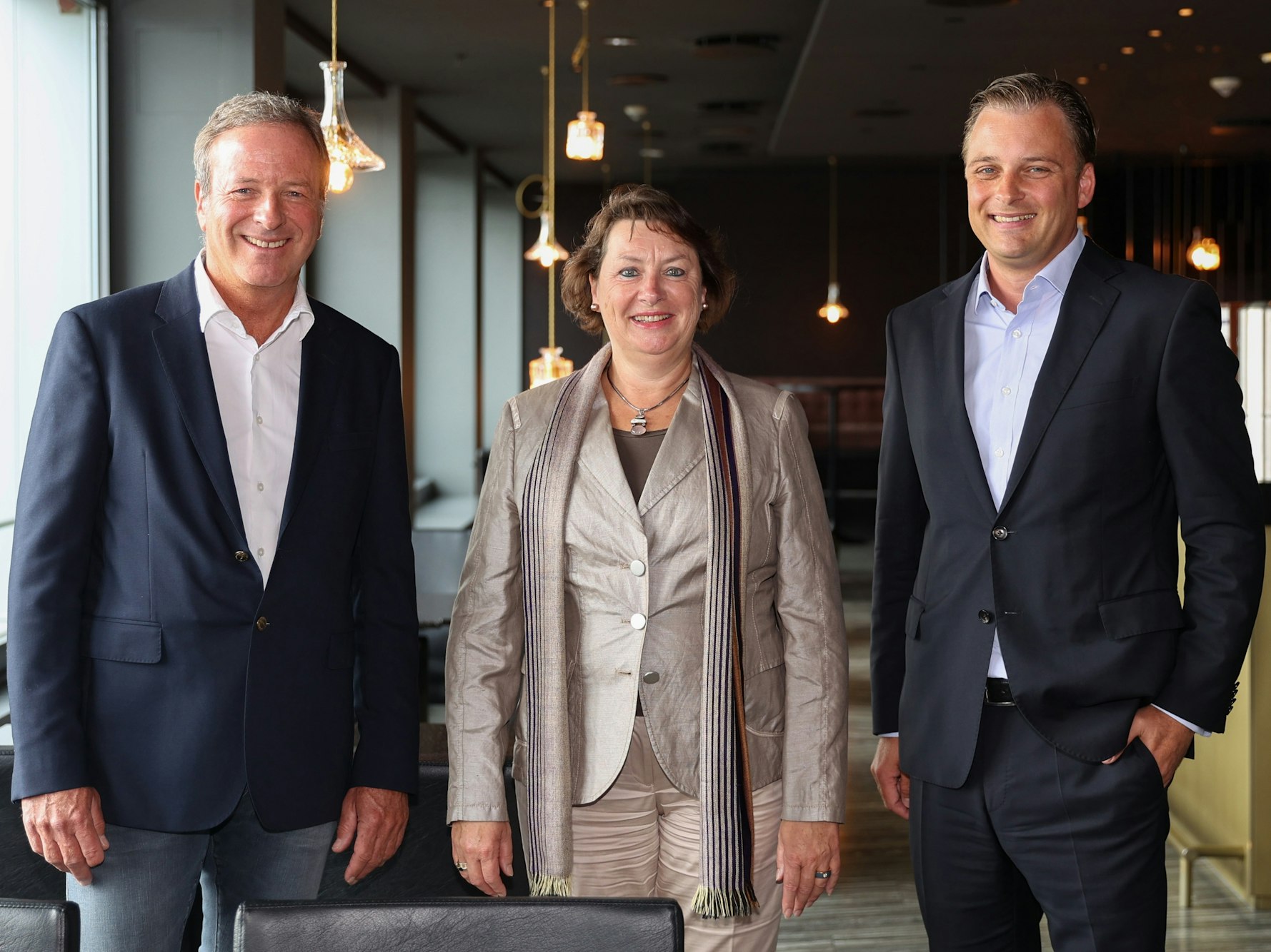 Michael Garvens, Anne Henk-Hollstein und Dr. Konrad Adenauer blicken im Pullman-Hotel in die Kamera.