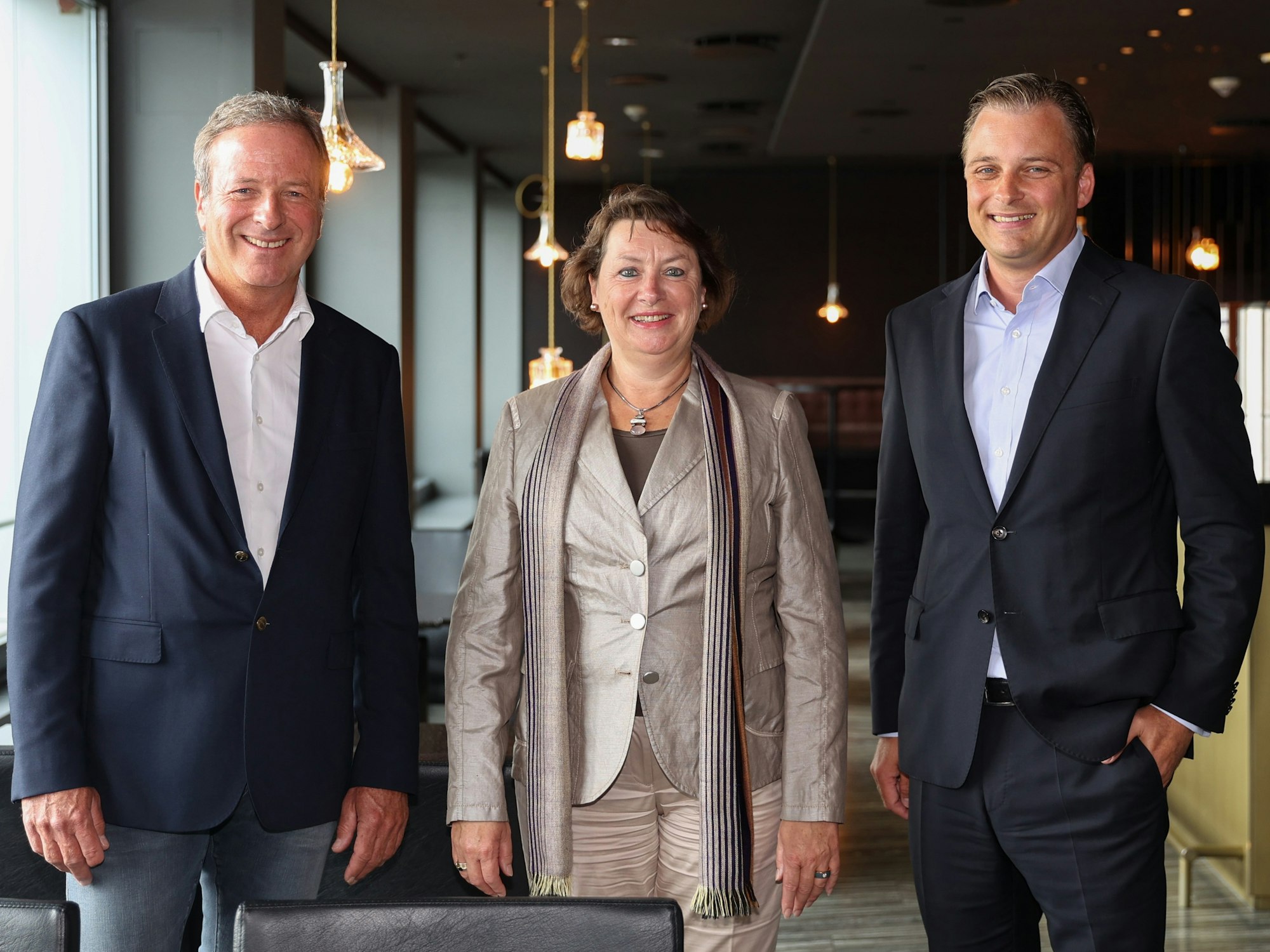 Michael Garvens, Anne Henk-Hollstein und Dr. Konrad Adenauer blicken im Pullman-Hotel in die Kamera.