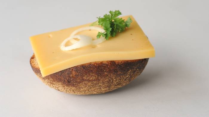 So lieben die Kölnerinnen und Kölner den Halven Hahn - mit Röggelchen. Ein halbes Roggenbrötchen ist mit einer Scheibe Käse, Zwiebelringen und Petersilie belegt.