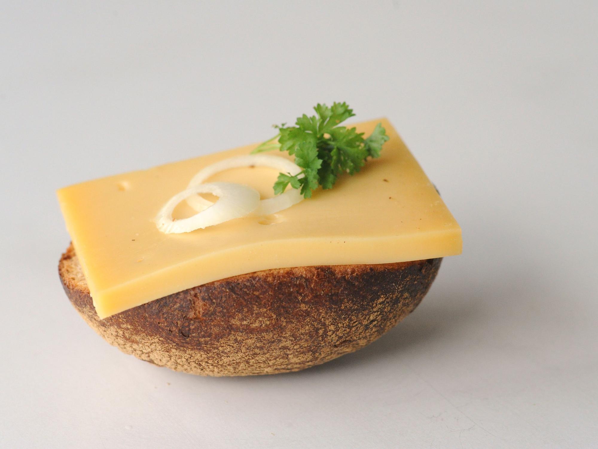 So lieben die Kölnerinnen und Kölner den Halven Hahn - mit Röggelchen. Ein halbes Roggenbrötchen ist mit einer Scheibe Käse, Zwiebelringen und Petersilie belegt.