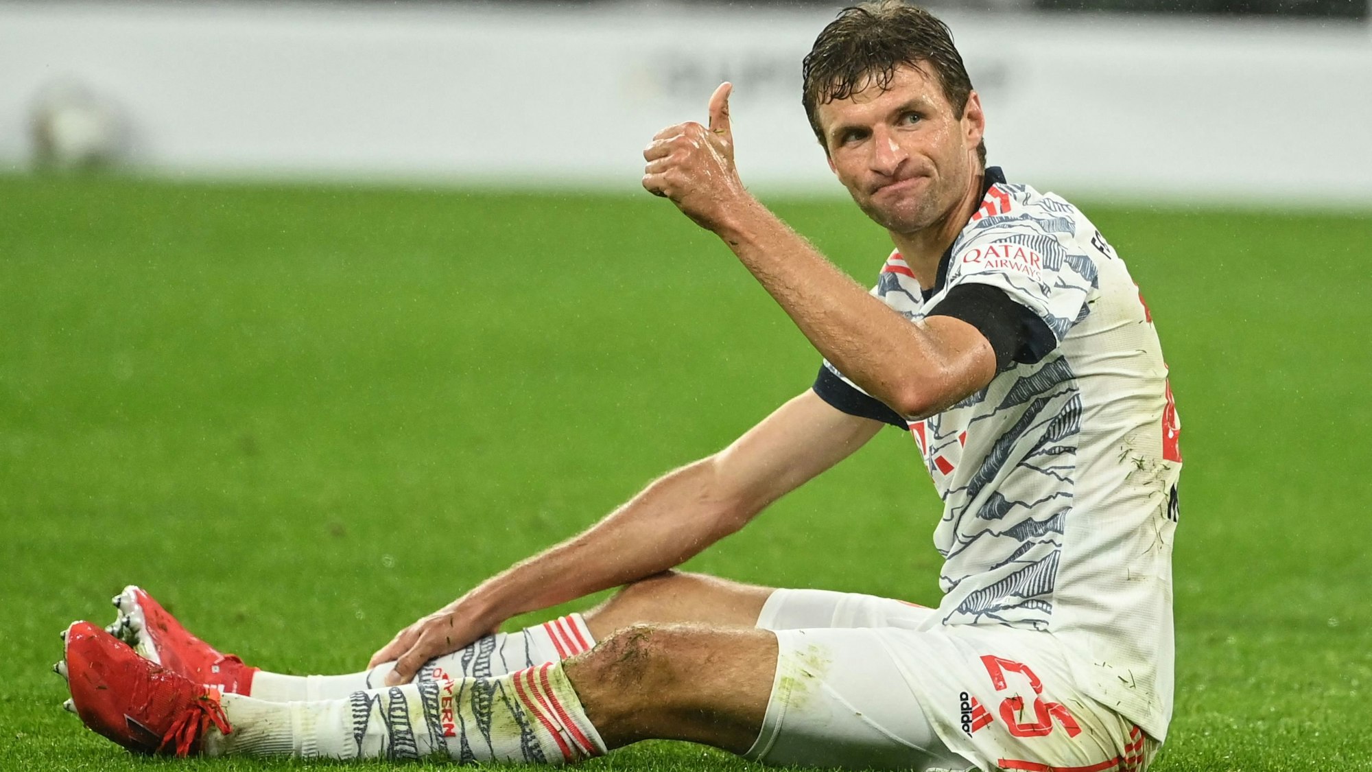 Thomas Müller sitzt auf dem Rasen und reckt den Daumen nach oben.