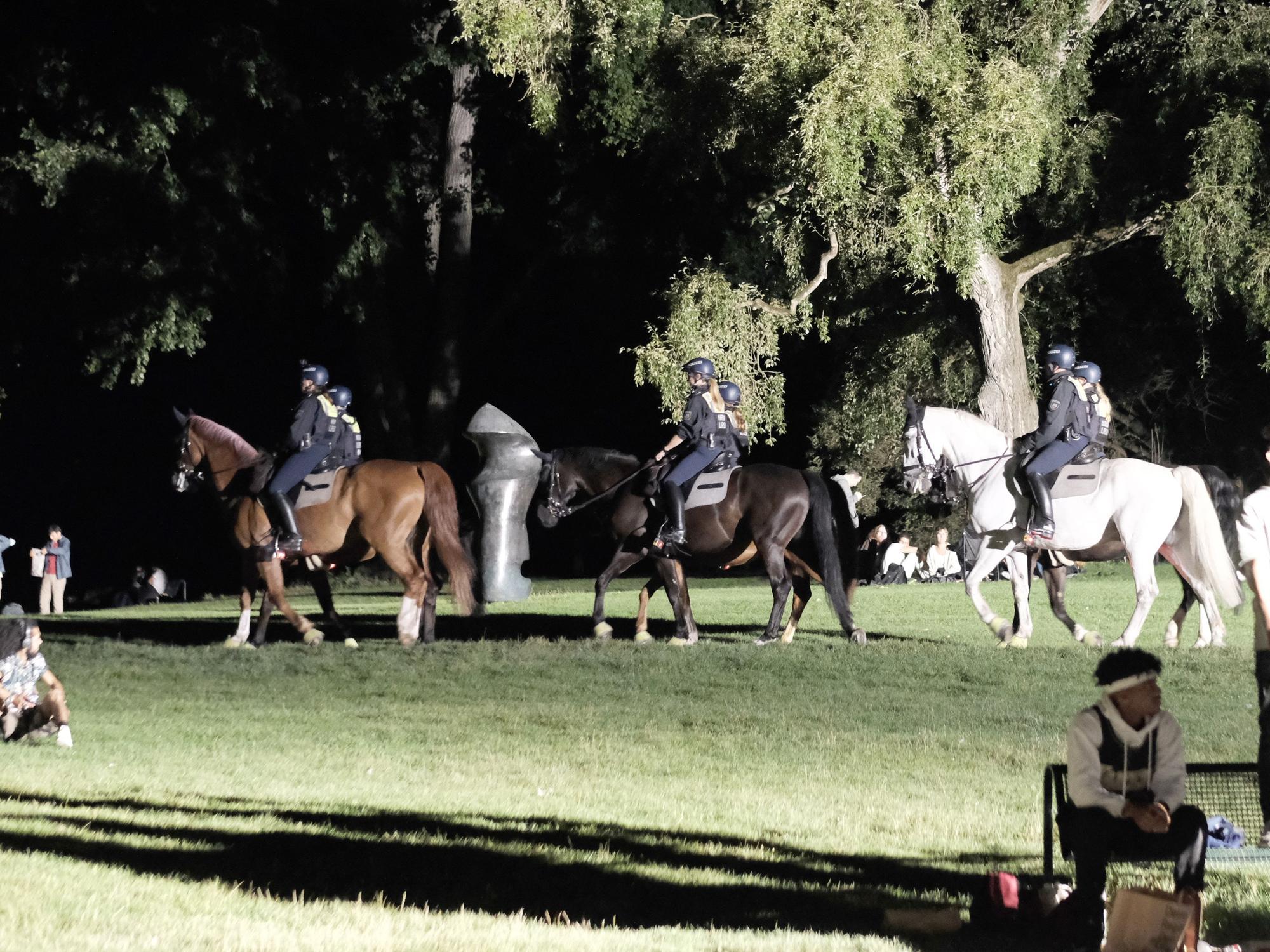 Polizisten auf Pferden reiten über die Grünfläche am Aachener Weiher.