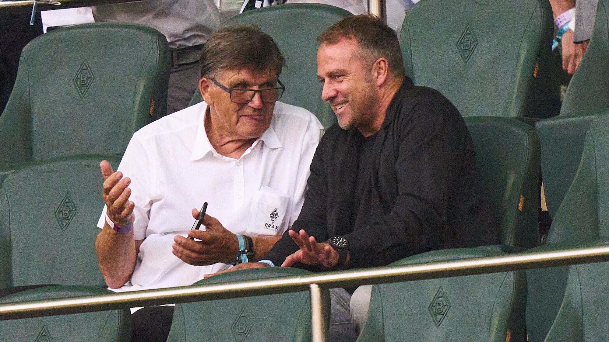 Hansi Flick sitzt in Mönchengladbach neben Hans Meyer auf der Tribüne.