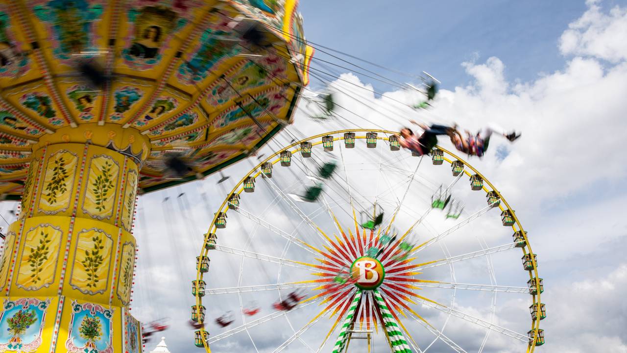 Besucherinnen und Besucher in einem Freizeitpark, im Hintergrund ein Riesenrad.