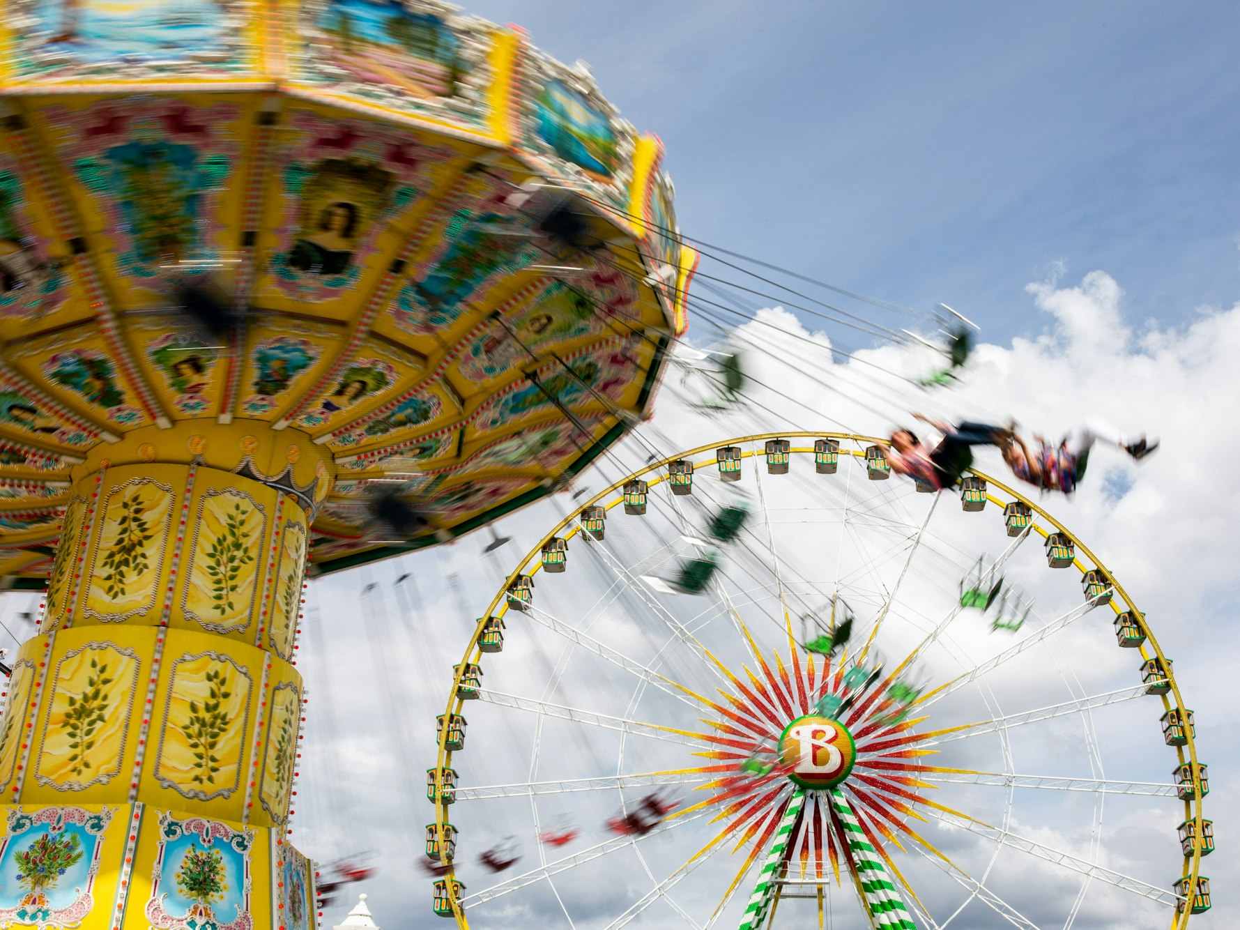 Besucherinnen und Besucher in einem Freizeitpark, im Hintergrund ein Riesenrad.