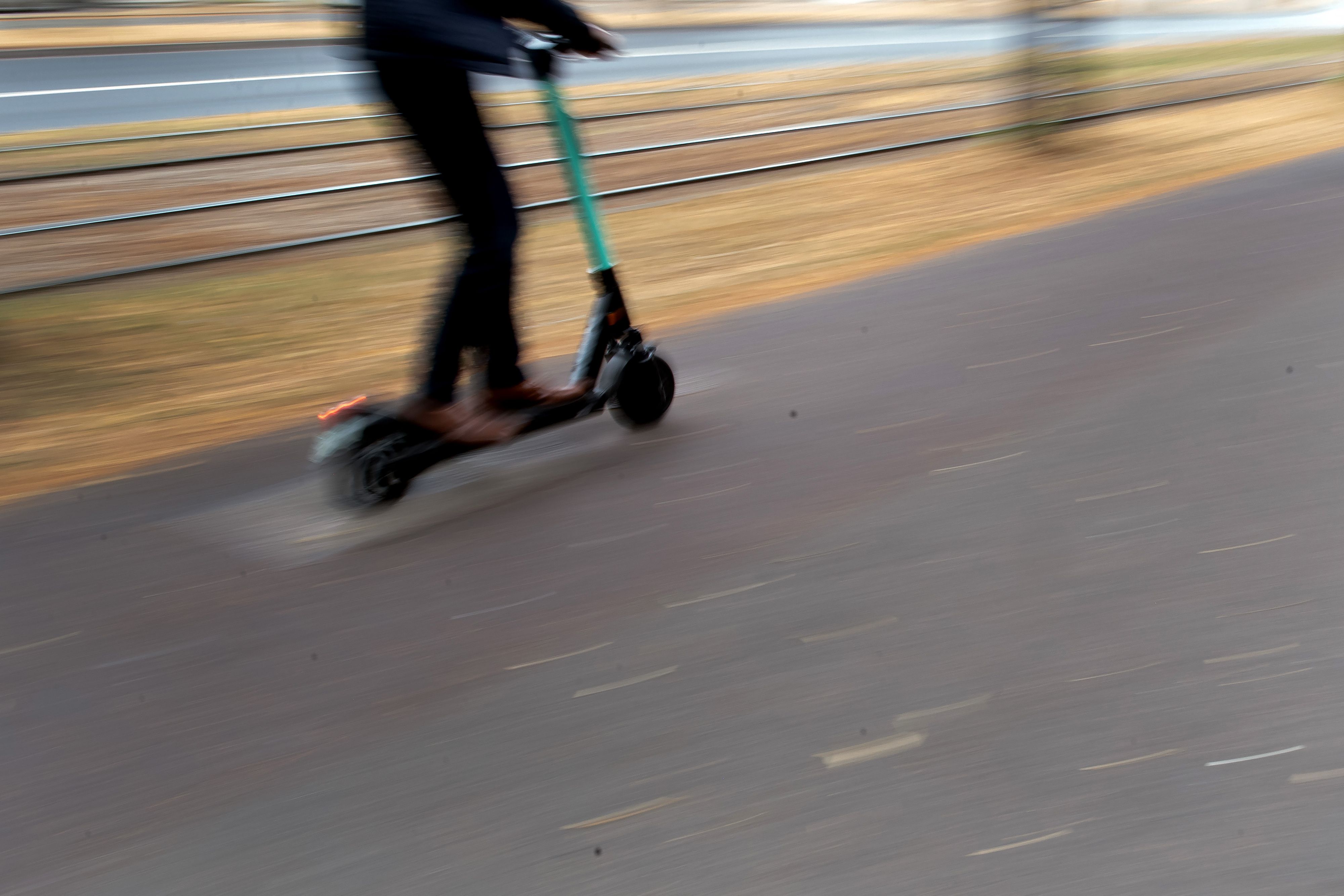 Ein Mann fährt mit einem E-Tretroller auf einem vom Gehweg abgetrennten Radweg neben Straßenbahnschienen durch die Stadt.