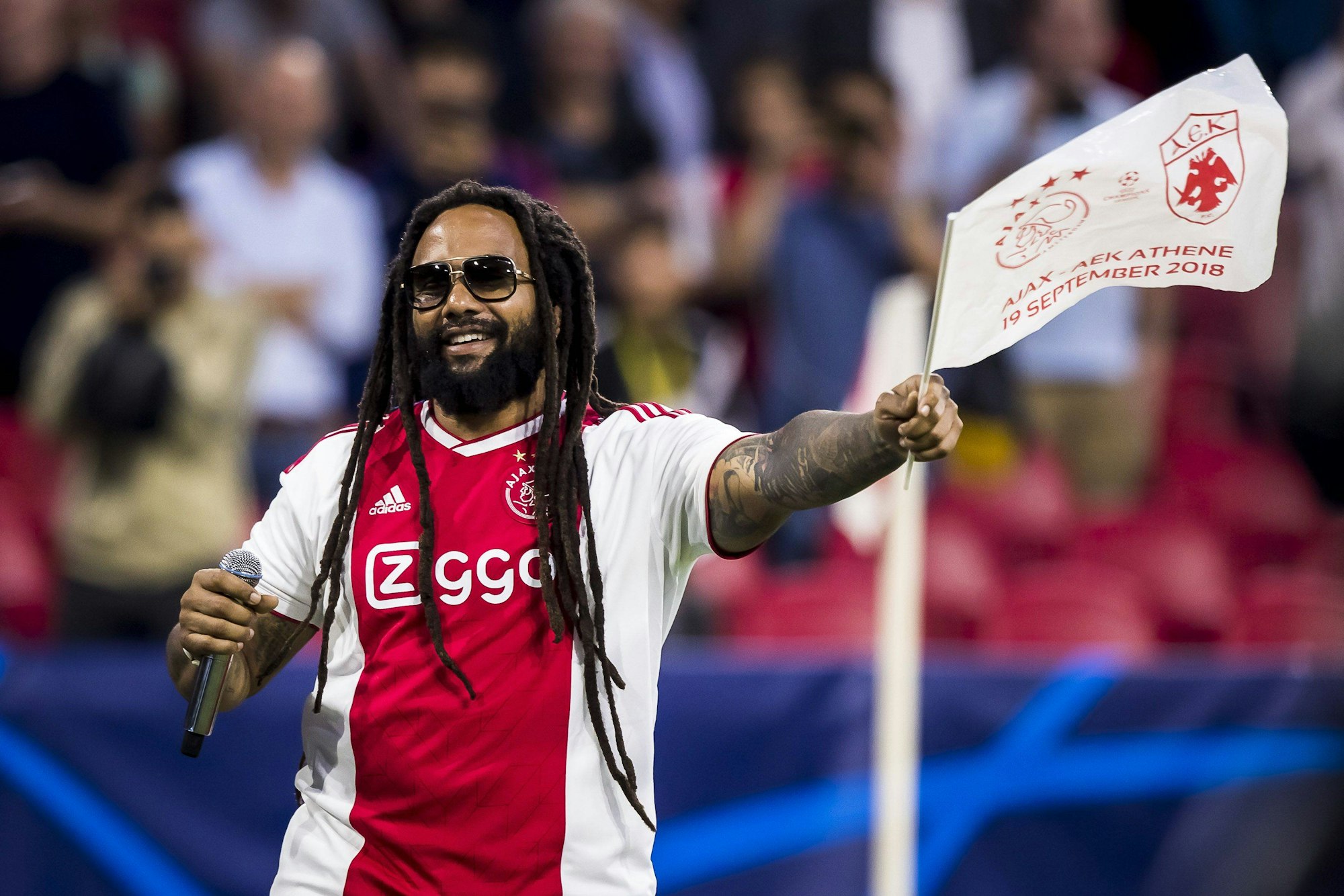 Bob Marleys Sohn Ky-Mani im Trikot von Ajax mit einem Mikro und einer Ajax-Fahne in der Hand.