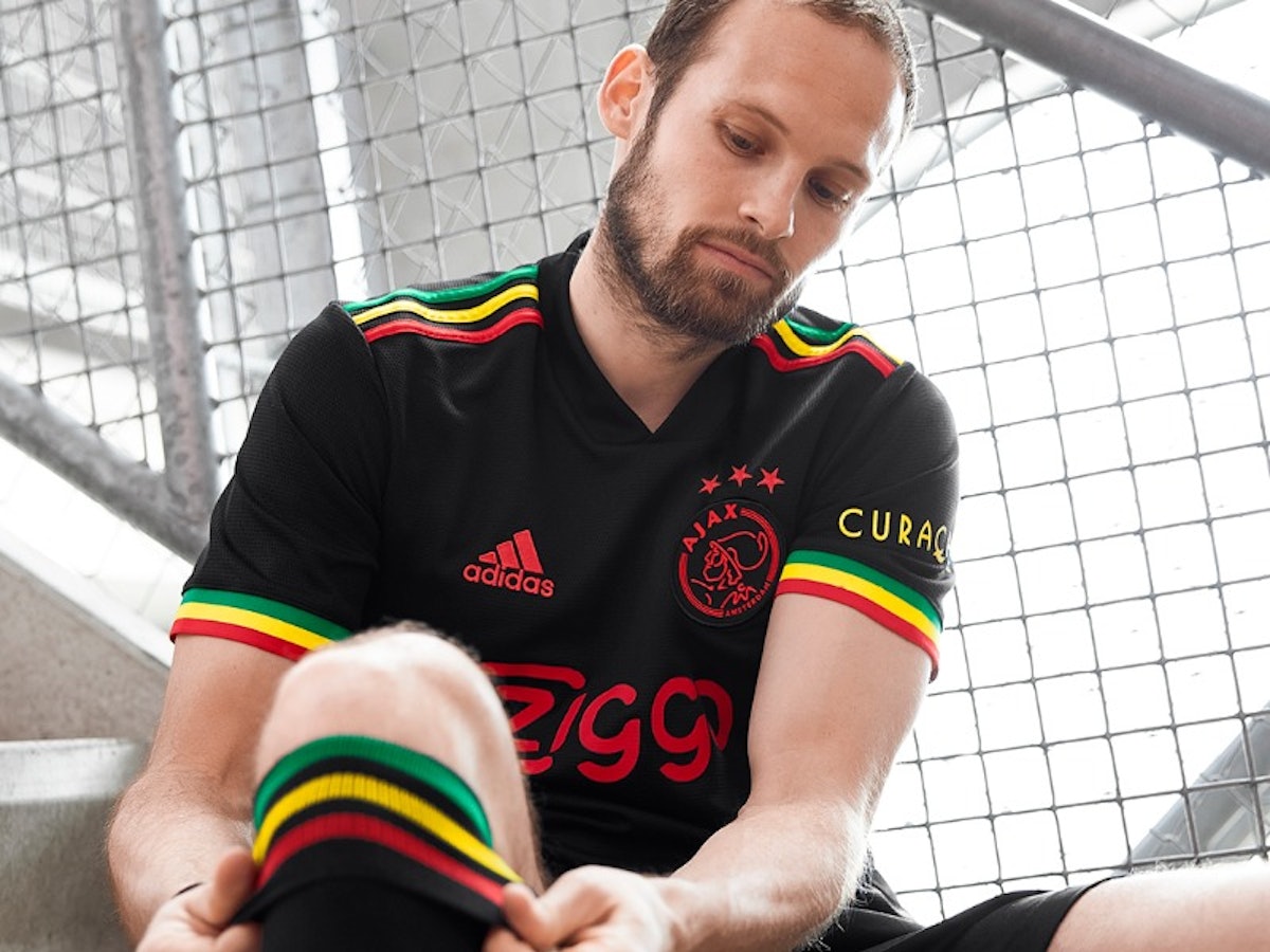 Ein Spieler sitzt im neuen schwarzen Trikot von Ajax auf einer Treppe und zieht sich die Stutzen zurecht.