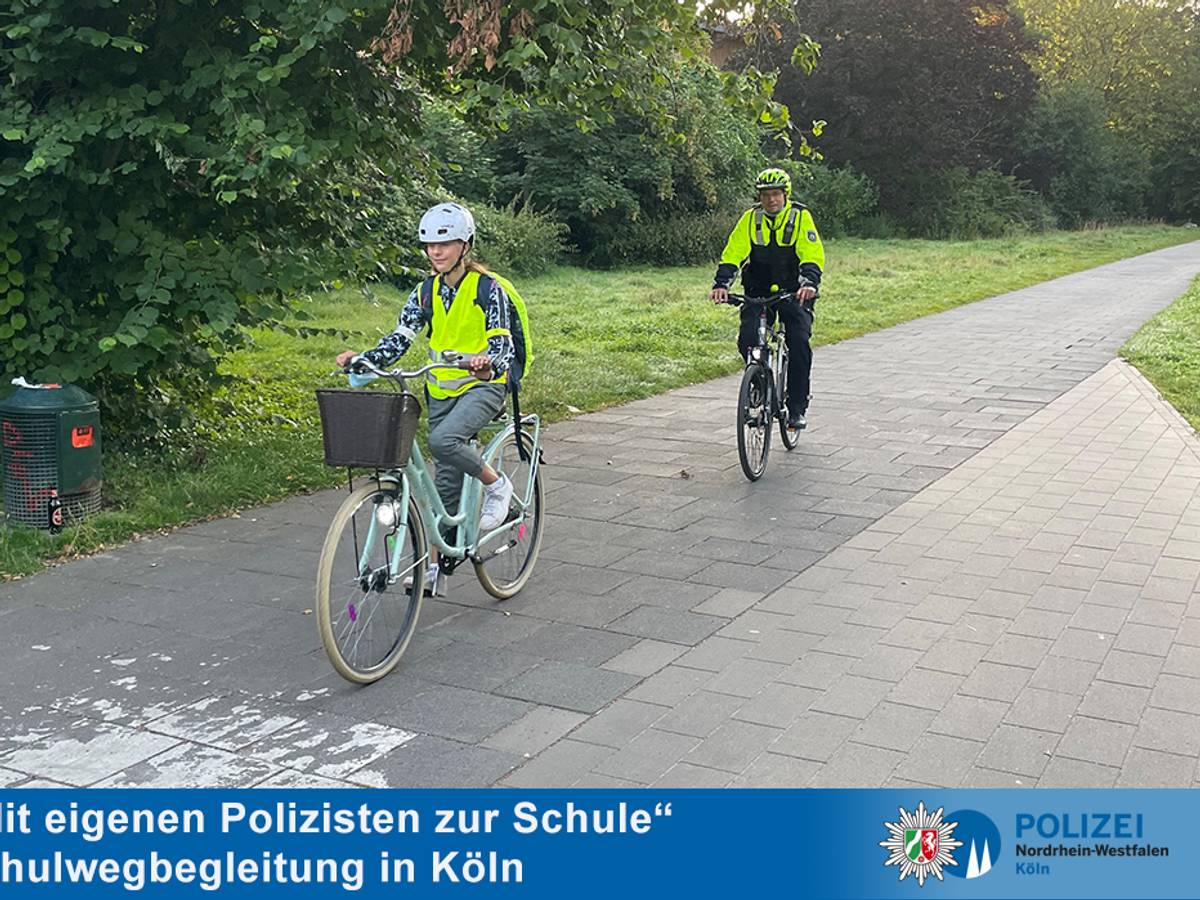 Eine Schülerin fährt in Warnweste vor einem Polizisten mit dem Rad.