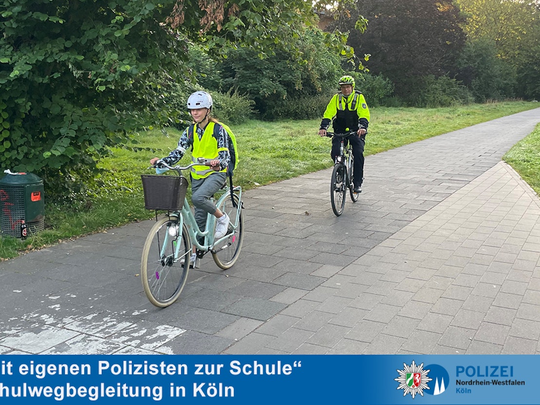 Eine Schülerin fährt in Warnweste vor einem Polizisten mit dem Rad.