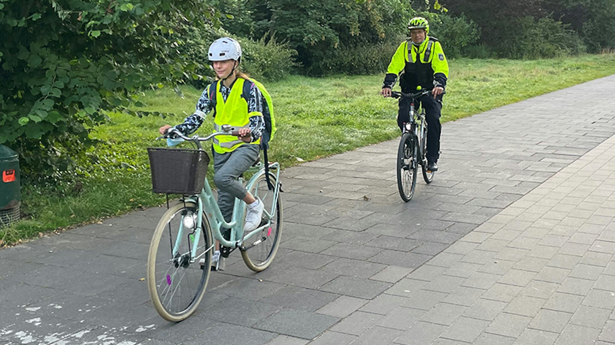 Eine Schülerin fährt in Warnweste vor einem Polizisten mit dem Rad.