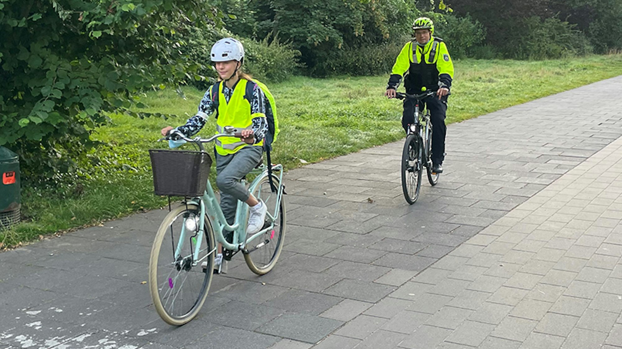 Eine Schülerin fährt in Warnweste vor einem Polizisten mit dem Rad.