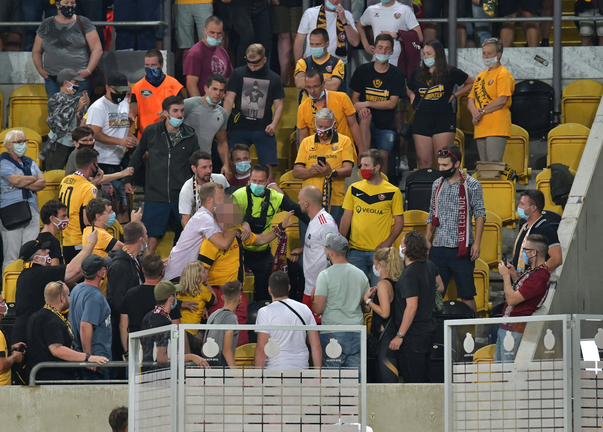 Toni Leistner steht auf der Tribüne inmitten von Dresden-Fans und baut sich vor einem Fan auf, der von einem anderen Fan zurückgehalten wird.