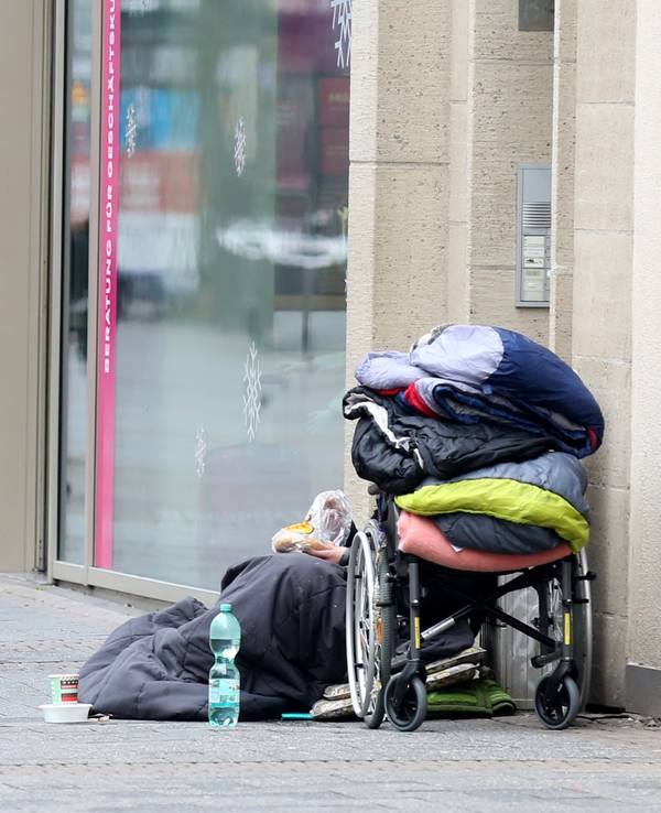 Ein Obdachloser sitzt in der Kölner Fußgängerzone vor einem Geschäft.