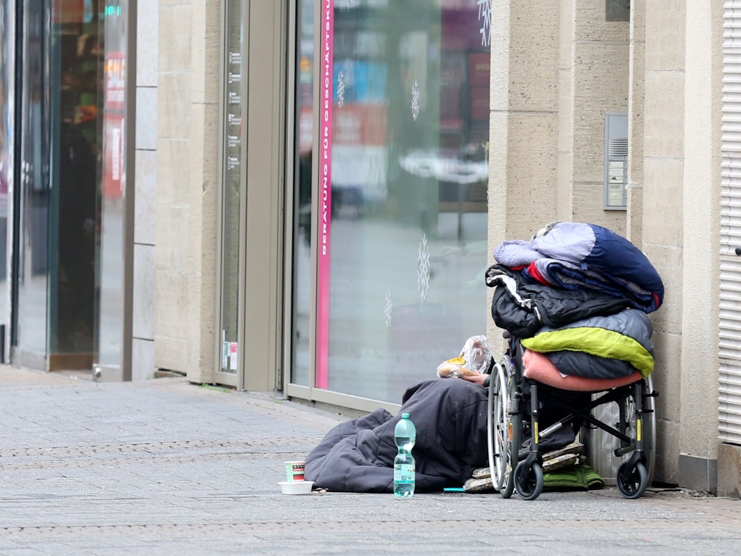 Ein Obdachloser sitzt in der Kölner Fußgängerzone vor einem Geschäft.