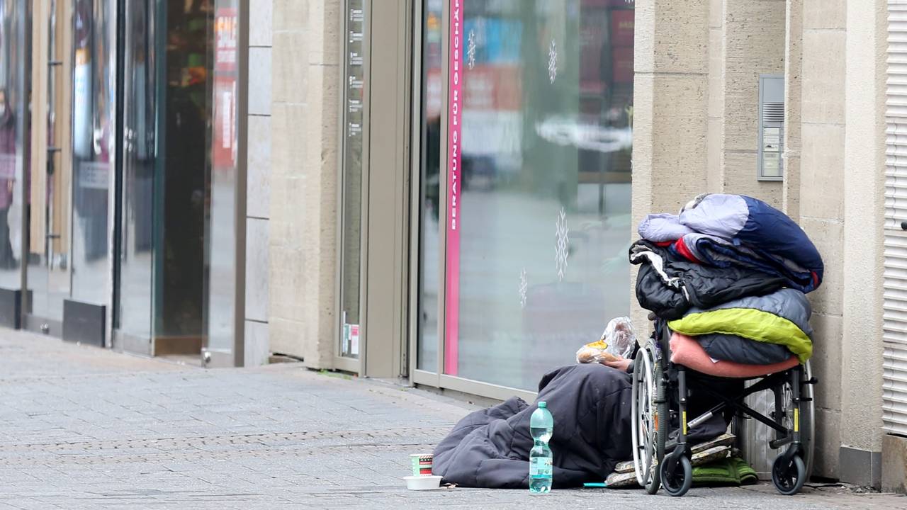 Ein Obdachloser sitzt in der Kölner Fußgängerzone vor einem Geschäft.